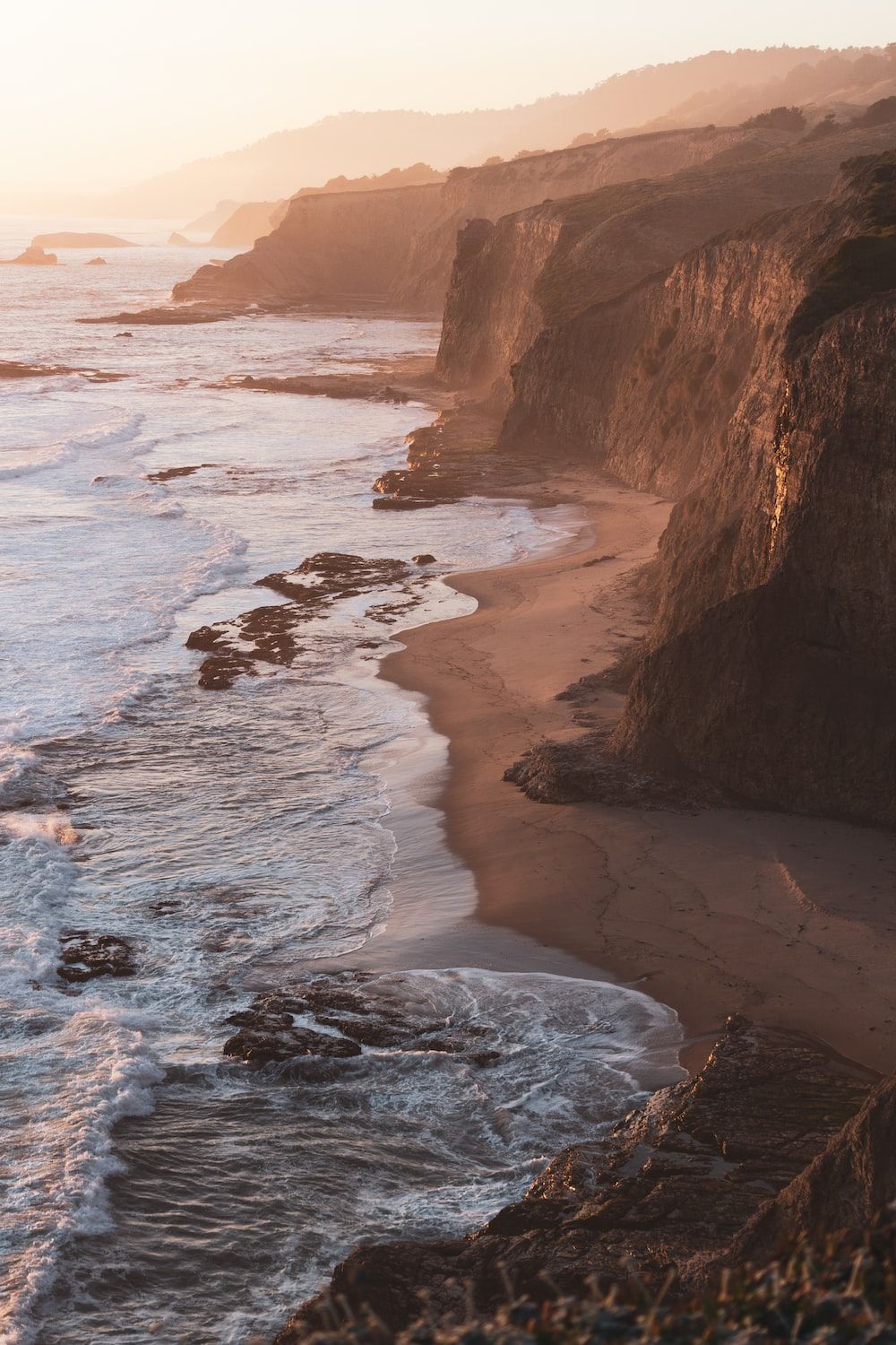 The sun is setting over a sandy beach with rocky cliffs. - California