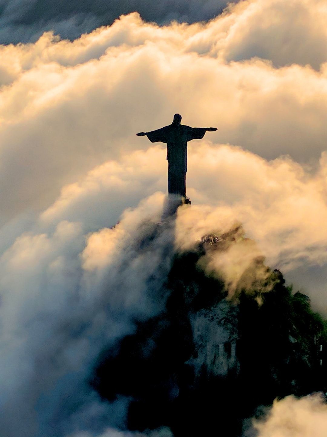 A statue of jesus on top is surrounded by clouds - Jesus