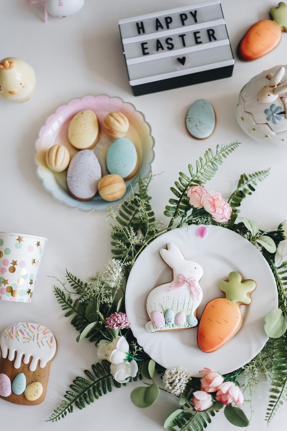 Easter table setting with bunny and carrot shaped cookies, macarons and a sign that says Happy Easter - Easter