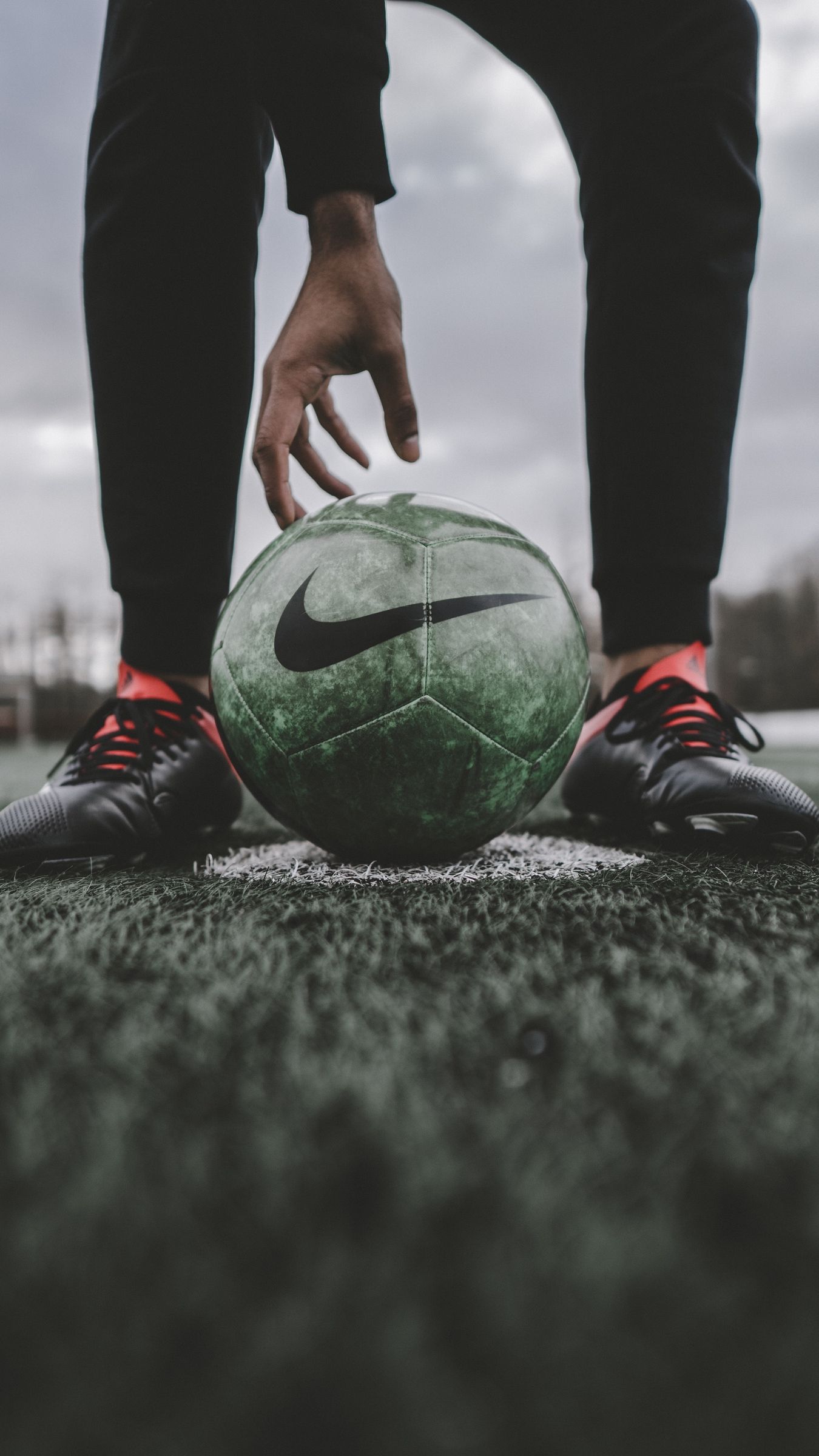 A person wearing black pants and red shoes is about to kick a green soccer ball on a field. - Soccer