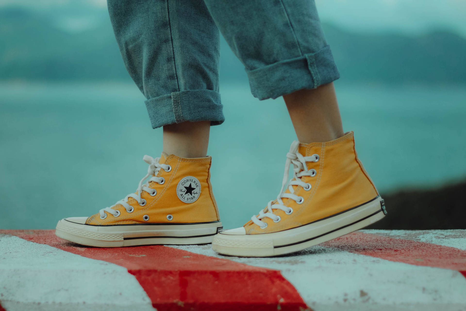 A person wearing yellow converse shoes standing on the edge of something - Shoes, Converse