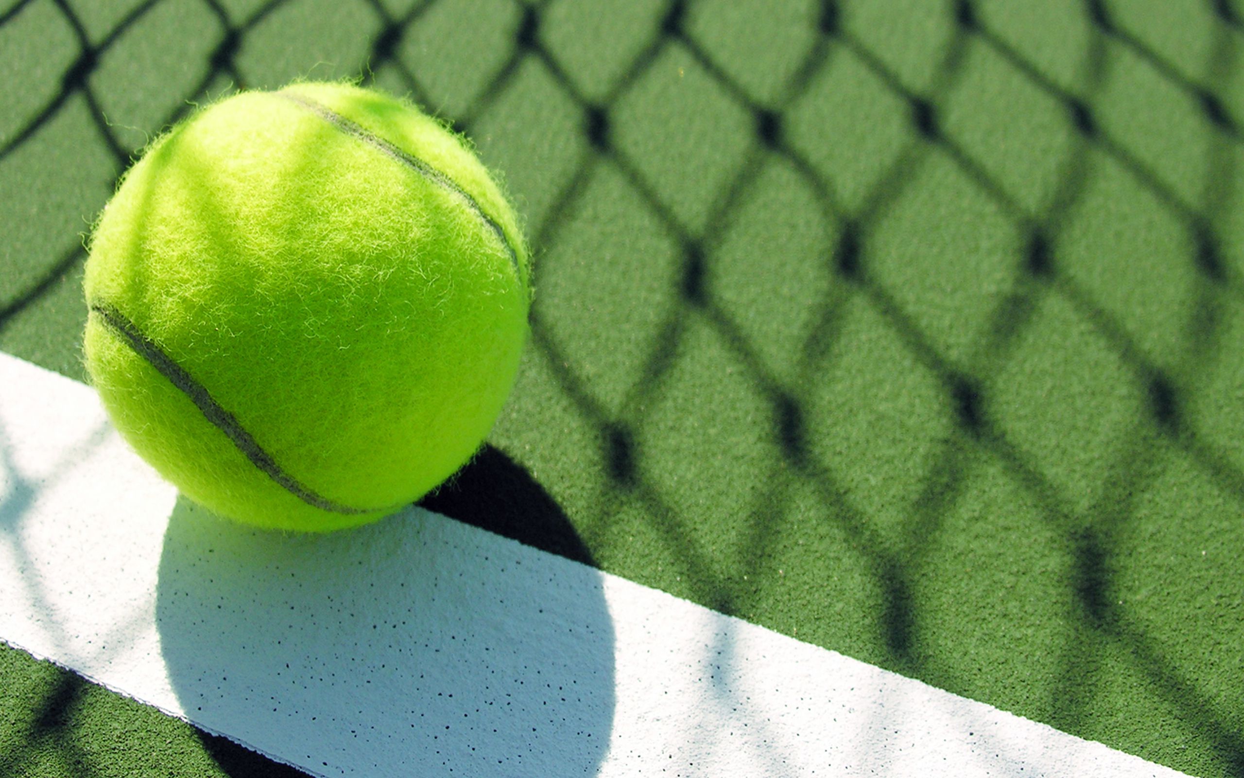 A tennis ball sits on the white line of a tennis court. - Tennis