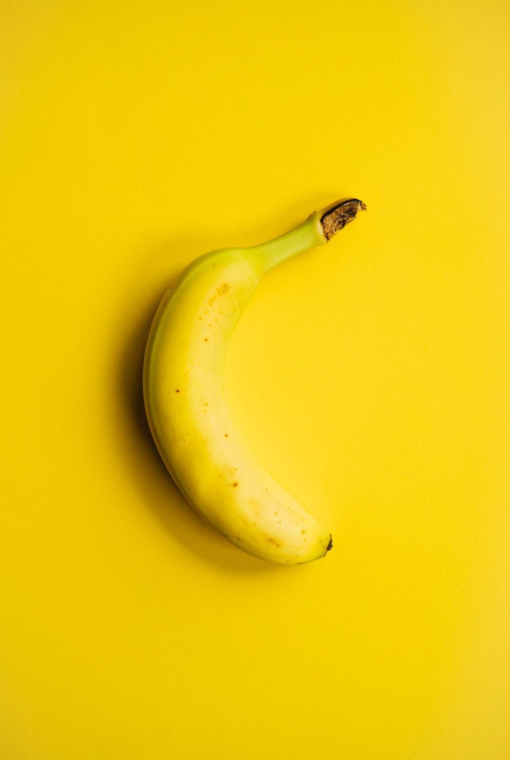 A single banana on top of yellow background - Banana