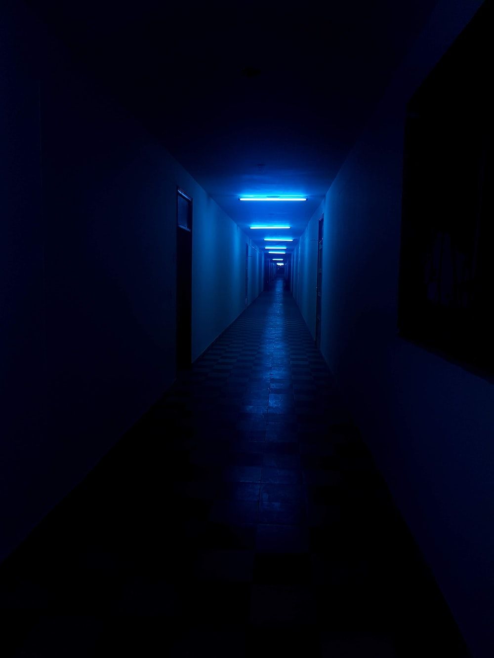 A hallway with blue lighting and black tiles - Neon blue, dark blue