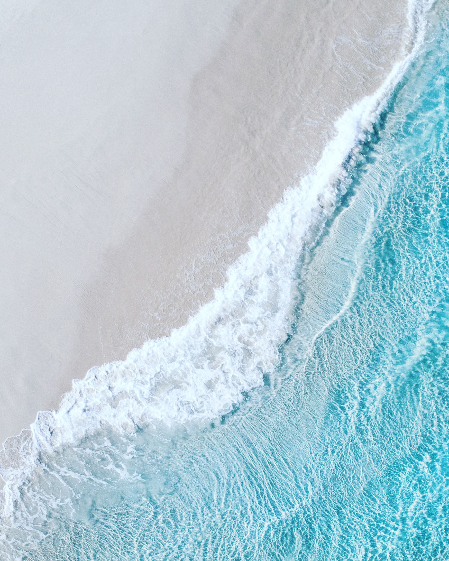 Aerial view of a wave breaking on a white sand beach - Light blue, pastel blue