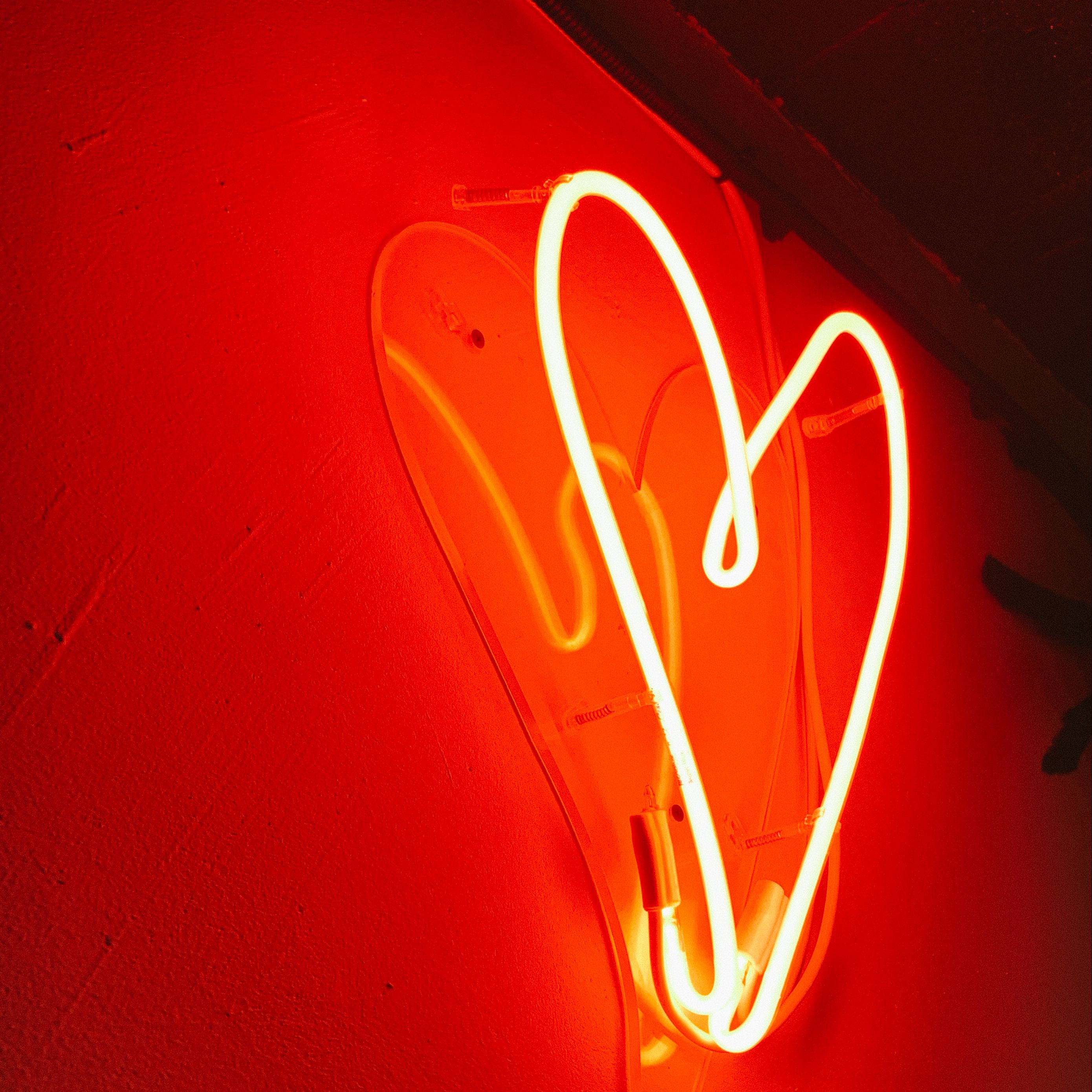 A heart-shaped neon sign glows against a red wall. - Light red