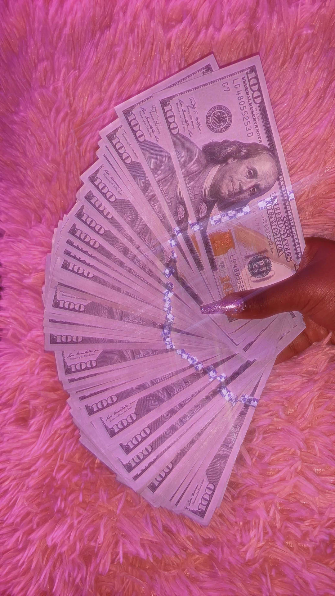 A person holding up some money on top of pink fur - Money