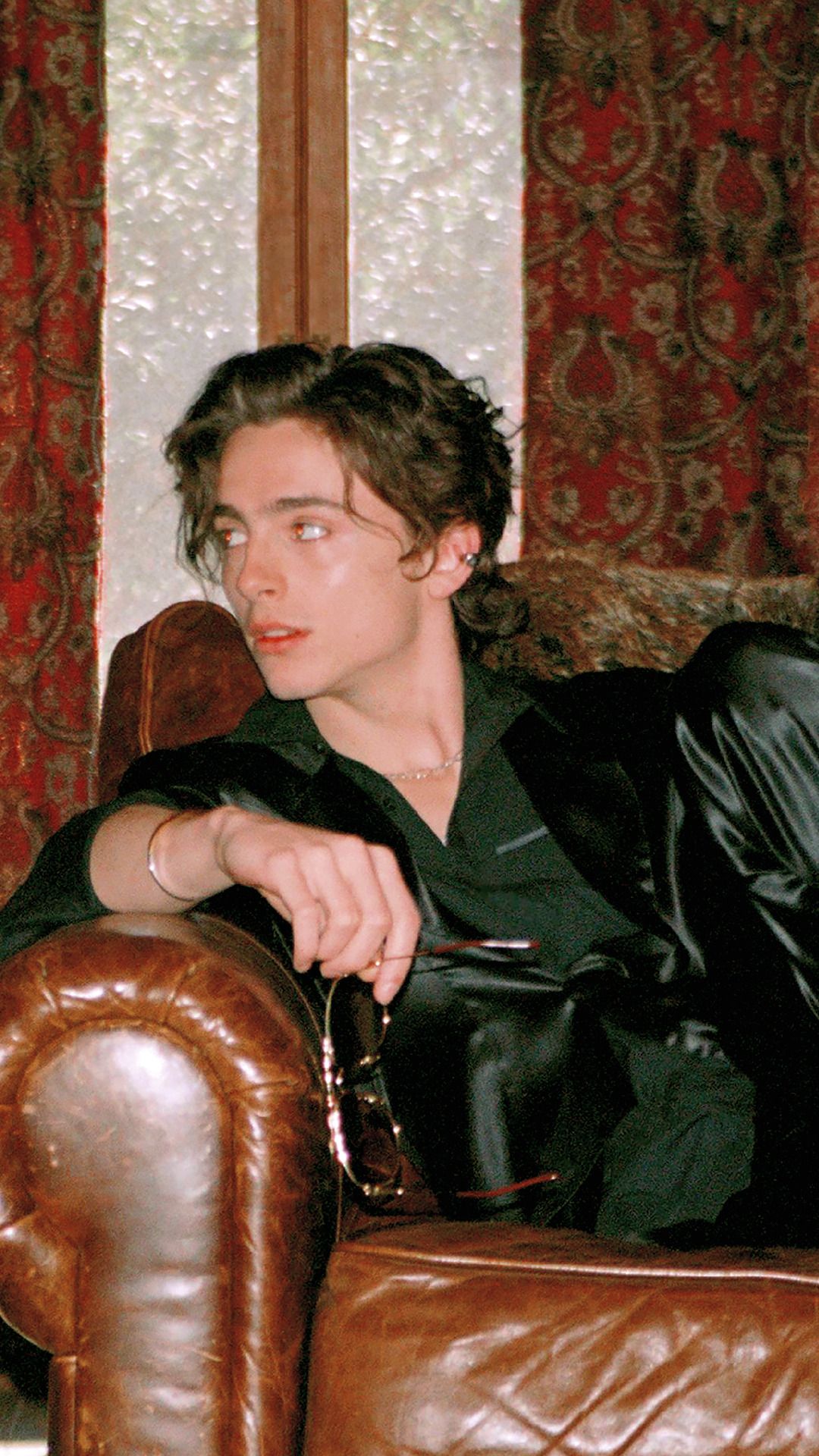 Timothee Chalamet in a black suit sitting on a brown couch - Timothee Chalamet