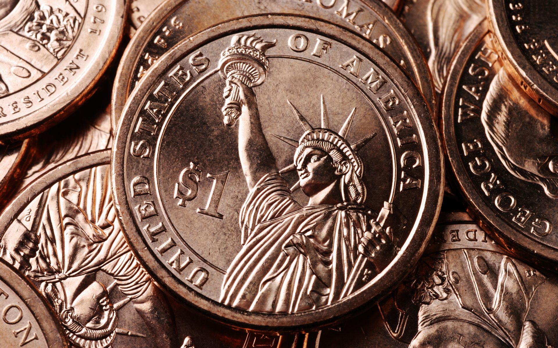 A close up of a pile of silver dollar coins with the statue of liberty on one of them. - Money