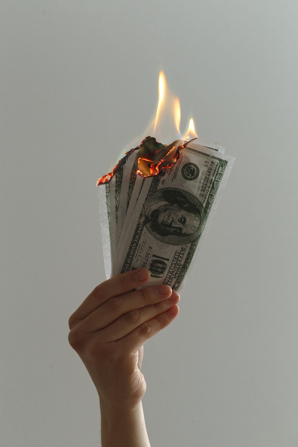 A person holding some burning money in their hand - Money
