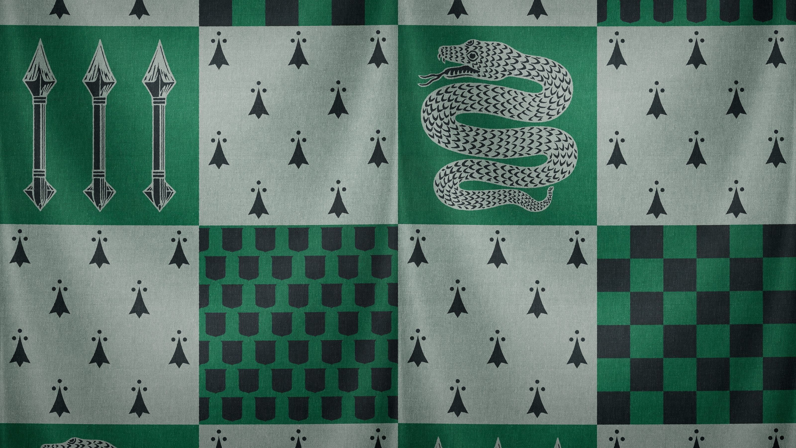 A close-up of the fabric of the Slytherin house robe, featuring the green and silver snake, the green and grey checkered pattern, and the green and grey pattern of quills and arrows. - Slytherin