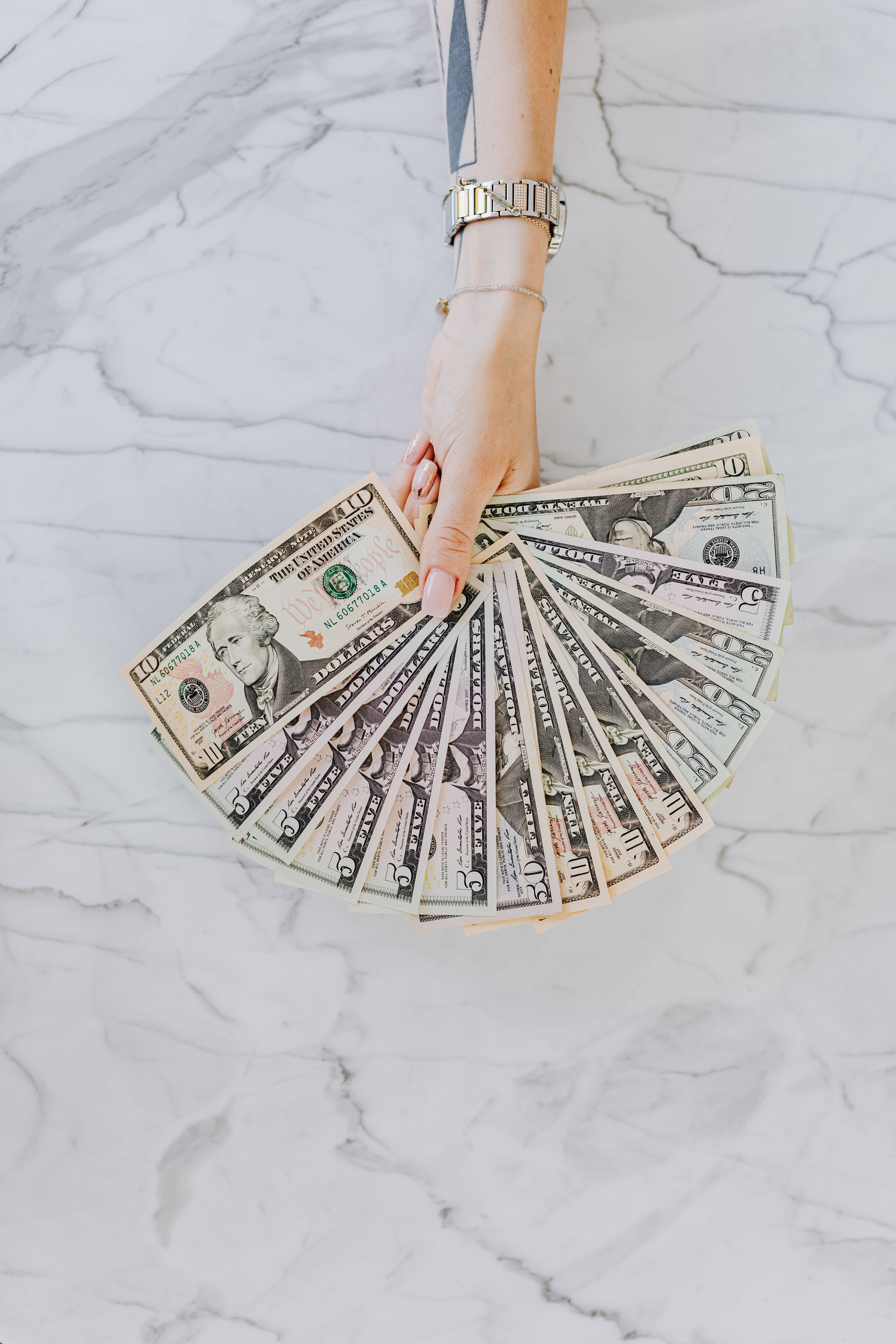 A woman's hand holding a fan of 20 dollar bills. - Money