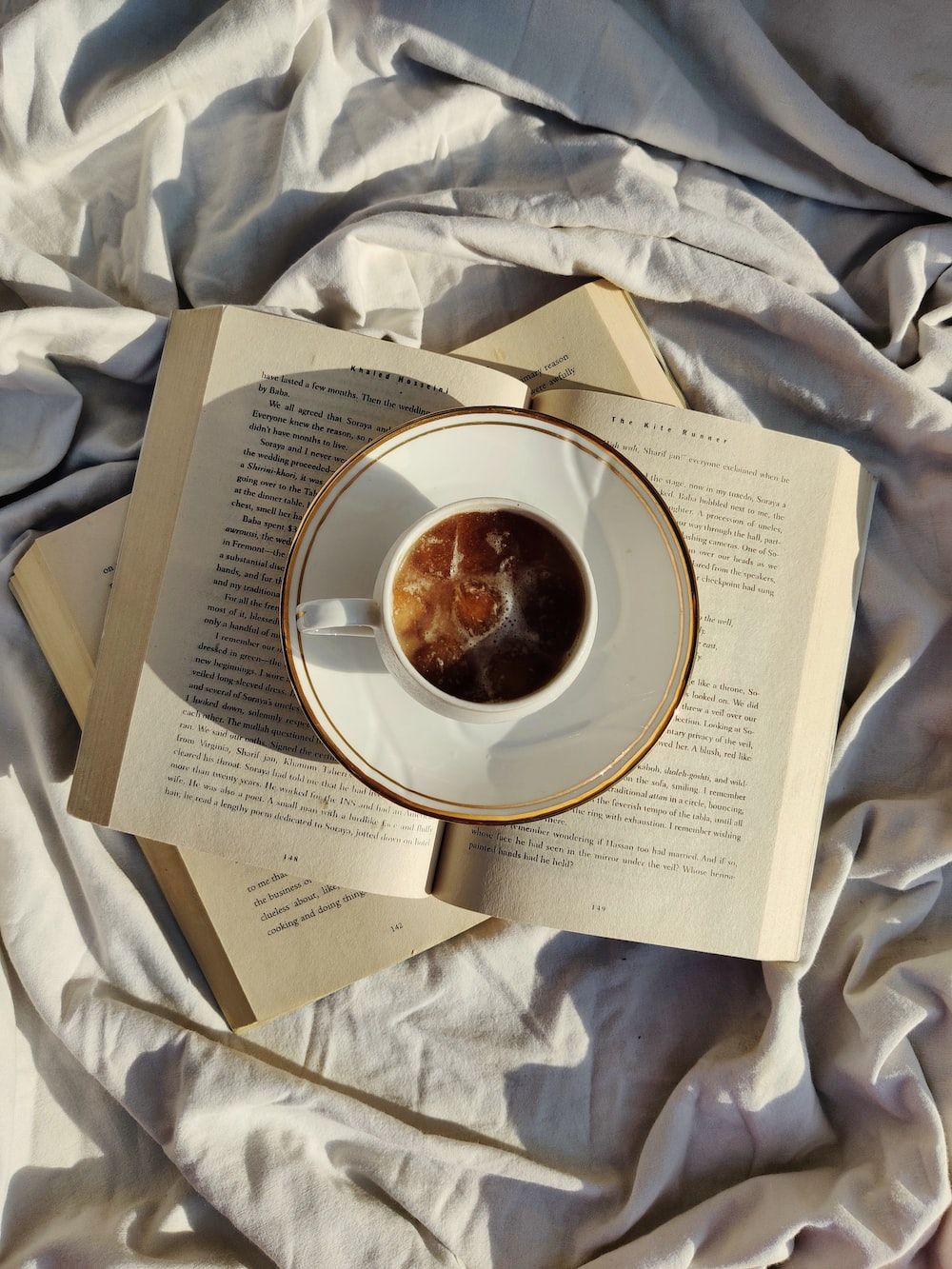A cup of coffee sits on top of an open book on a bed. - Vintage, coffee, retro