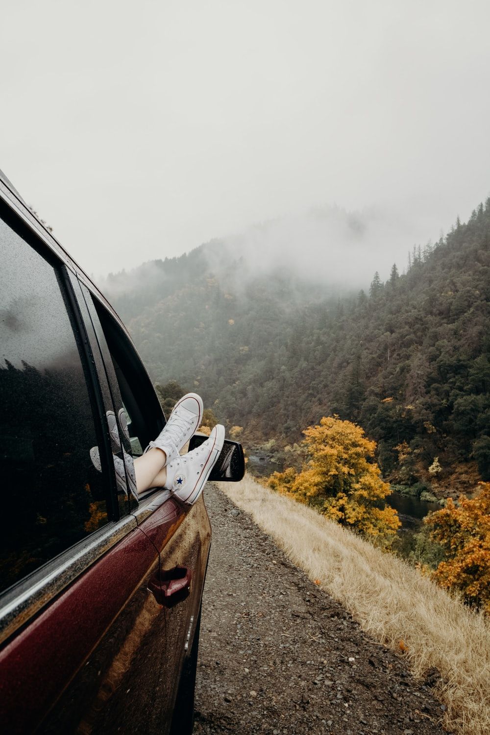 A person's feet sticking out of a car window with a foggy mountain in the background. - Travel