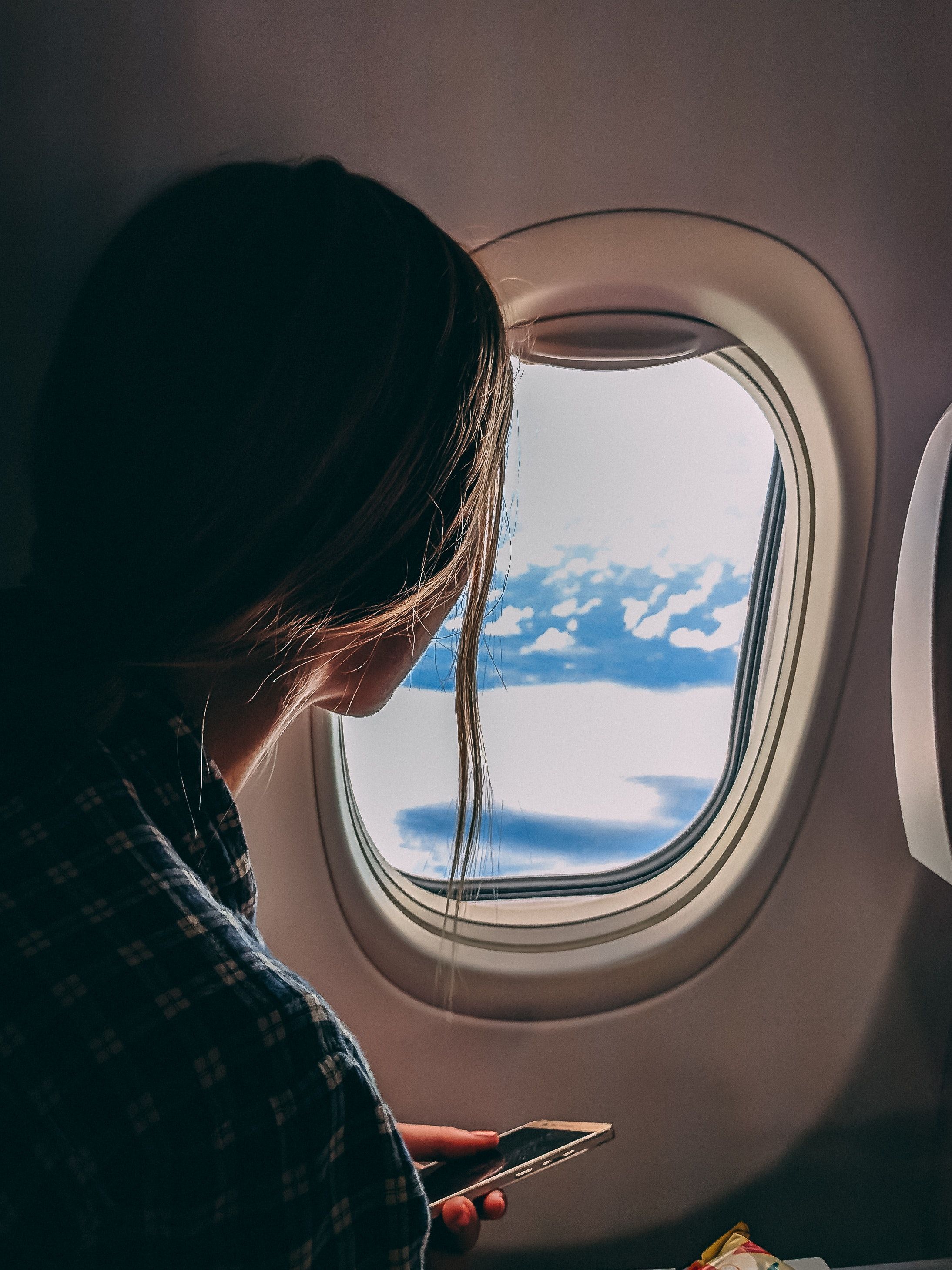 A woman looks out of a plane window at the clouds - Travel, airplane