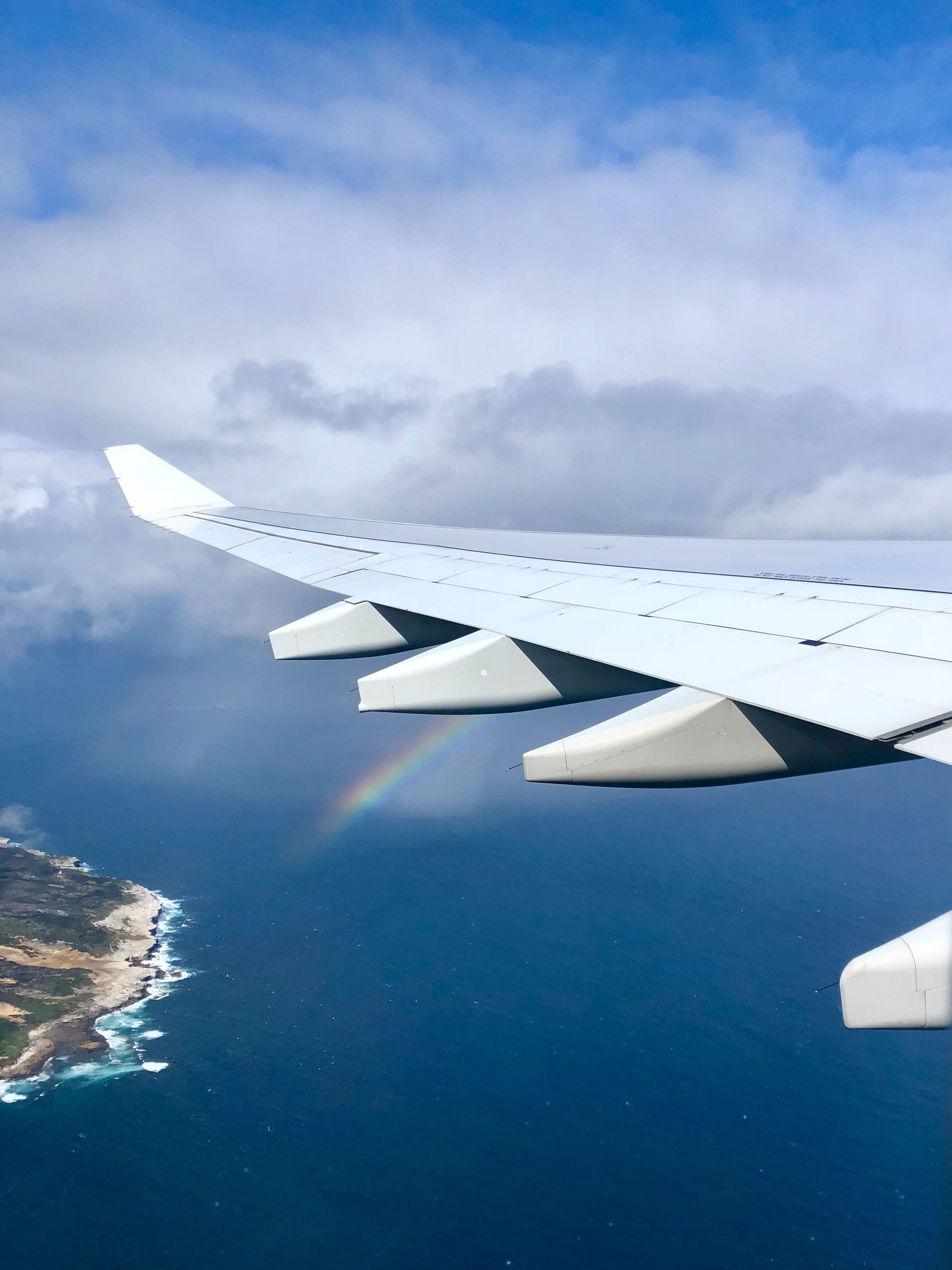 A view of a plane wing over the ocean with a rainbow below - Travel, airplane