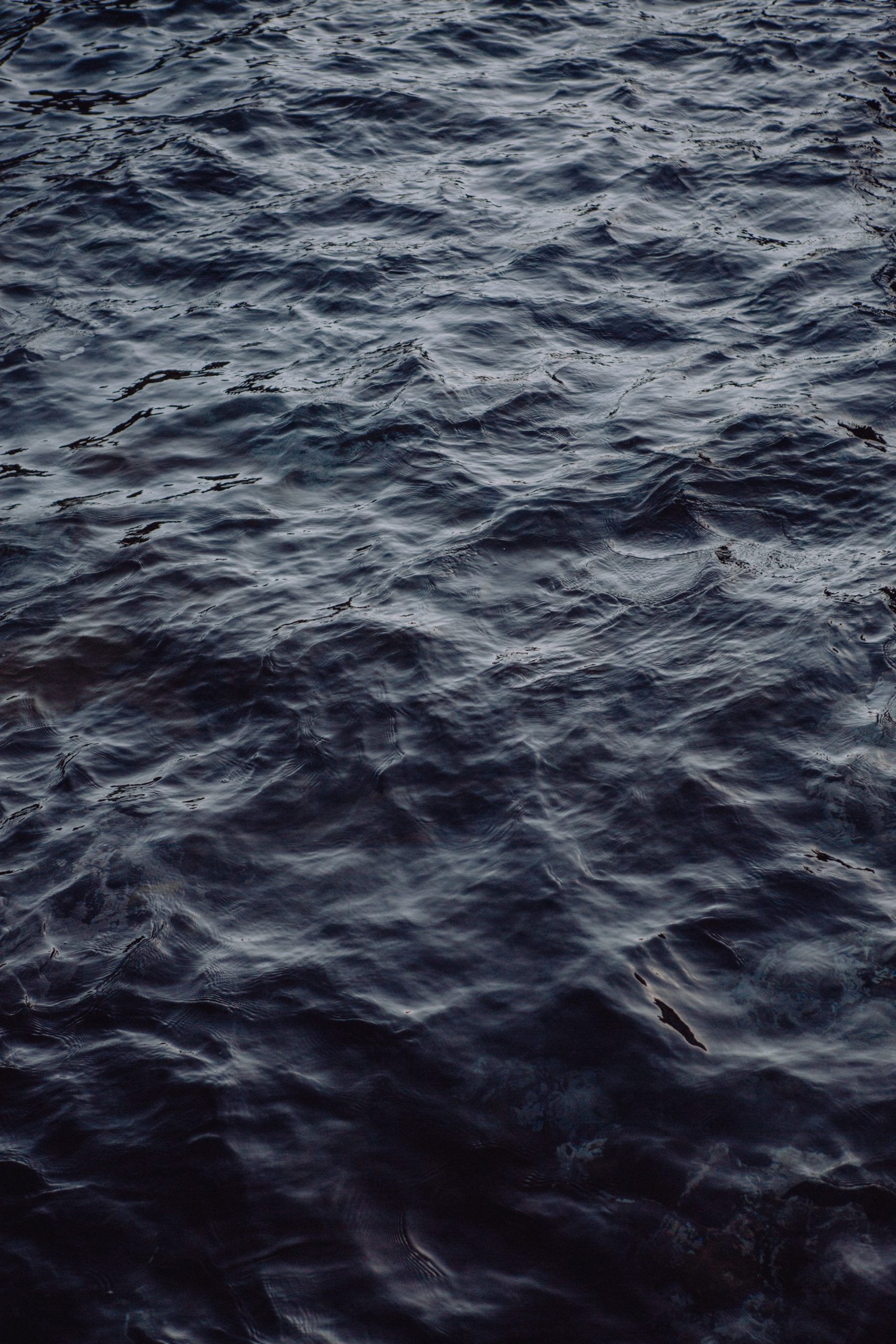 A dark blue and black water surface with small waves - Water