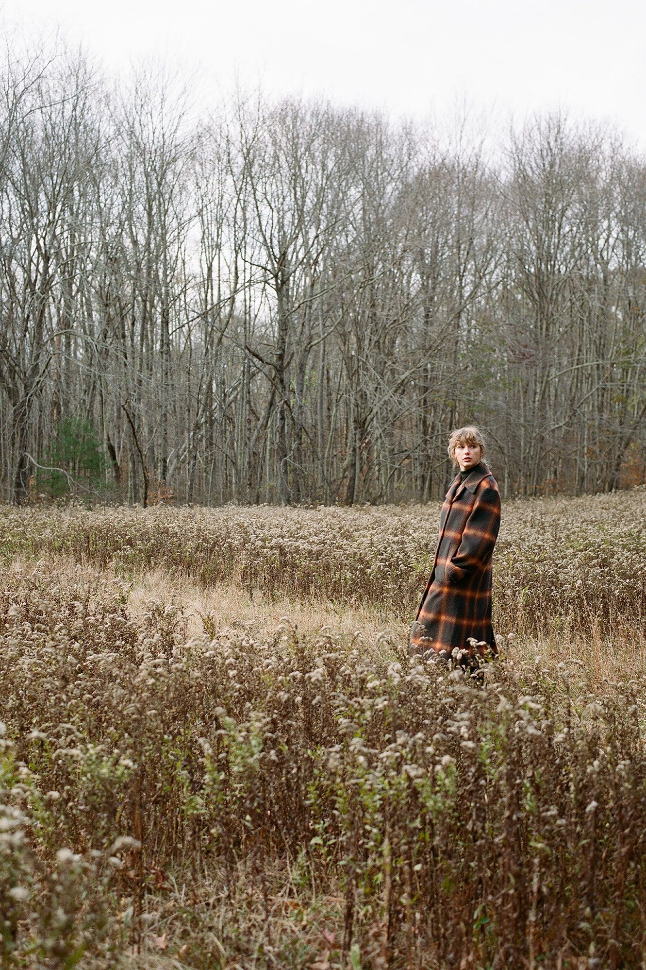 A man in plaid coat standing on grassy field - Taylor Swift