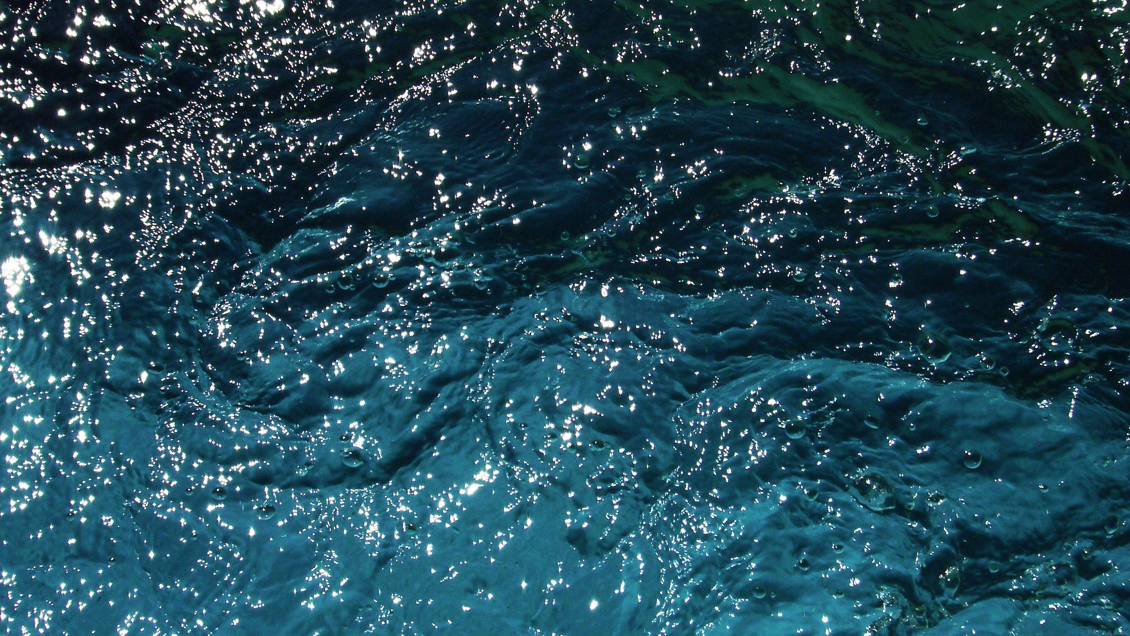 A close up of the water in a river, with ripples and sunlight shining through. - Water