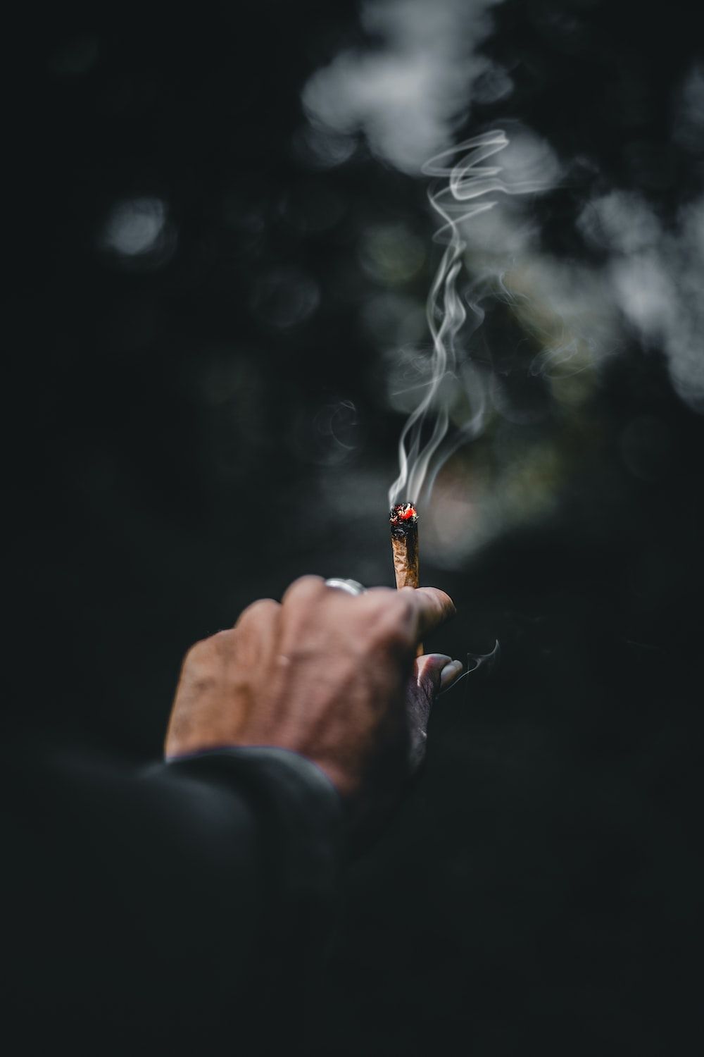 A hand holding a lit joint in the dark - Weed