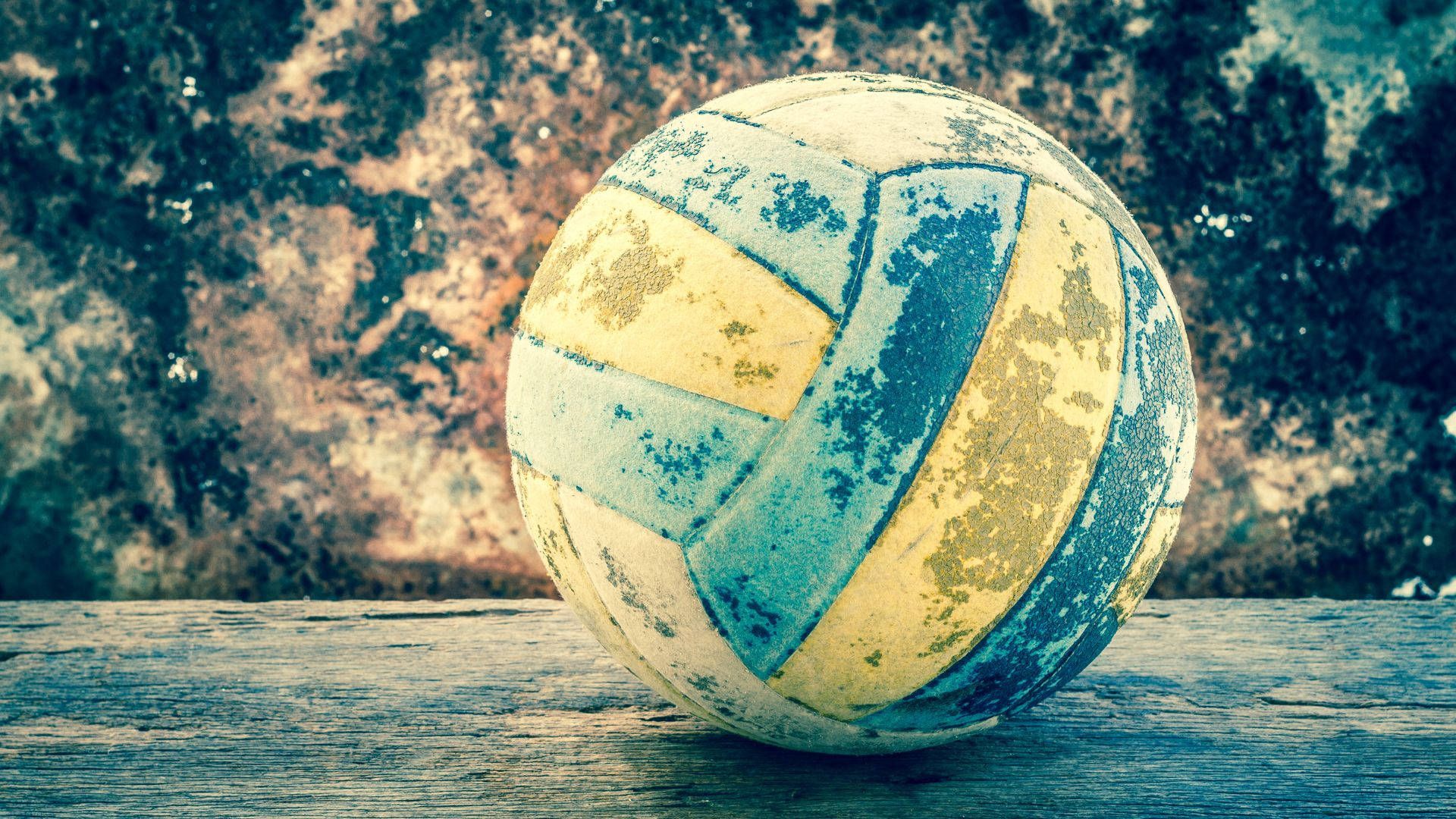 A blue and yellow ball sitting on the ground - Volleyball