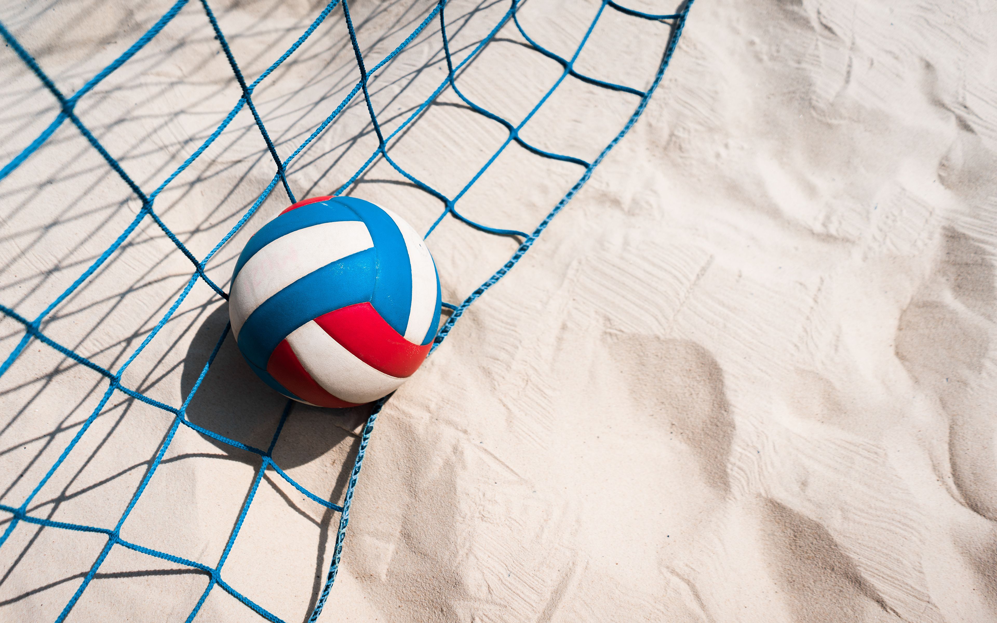 A volleyball in the sand next to a blue net. - Volleyball