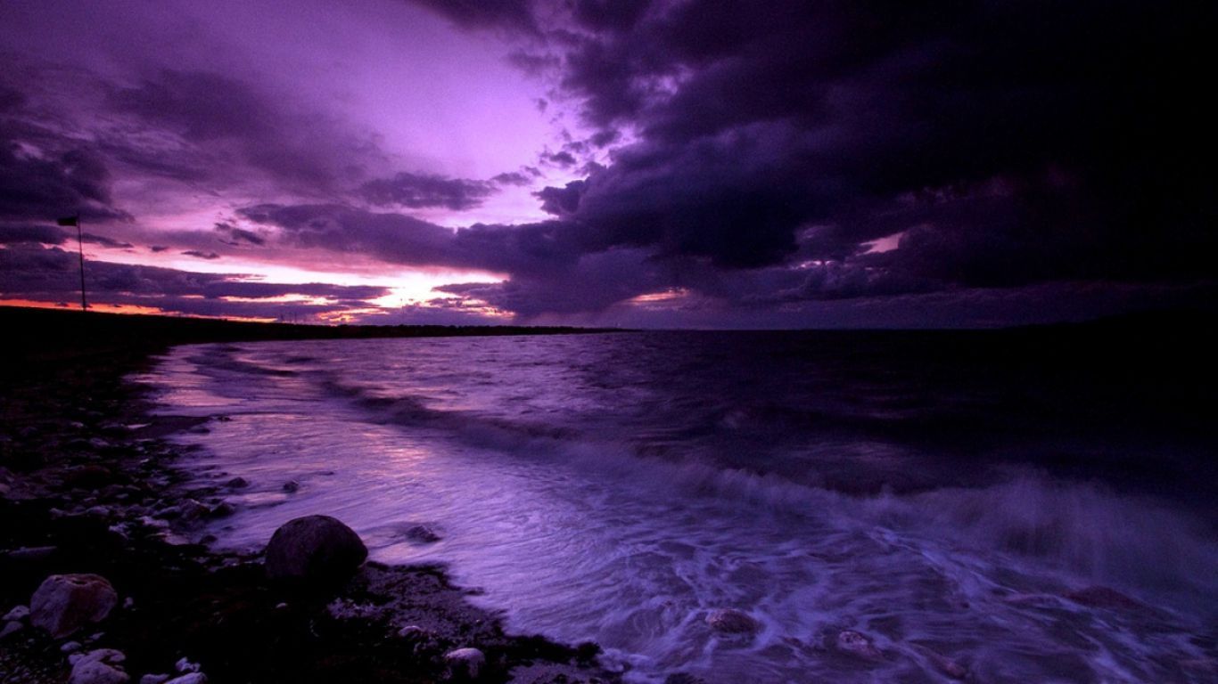 Purple sunset over the ocean with rocks in the foreground. - 1366x768