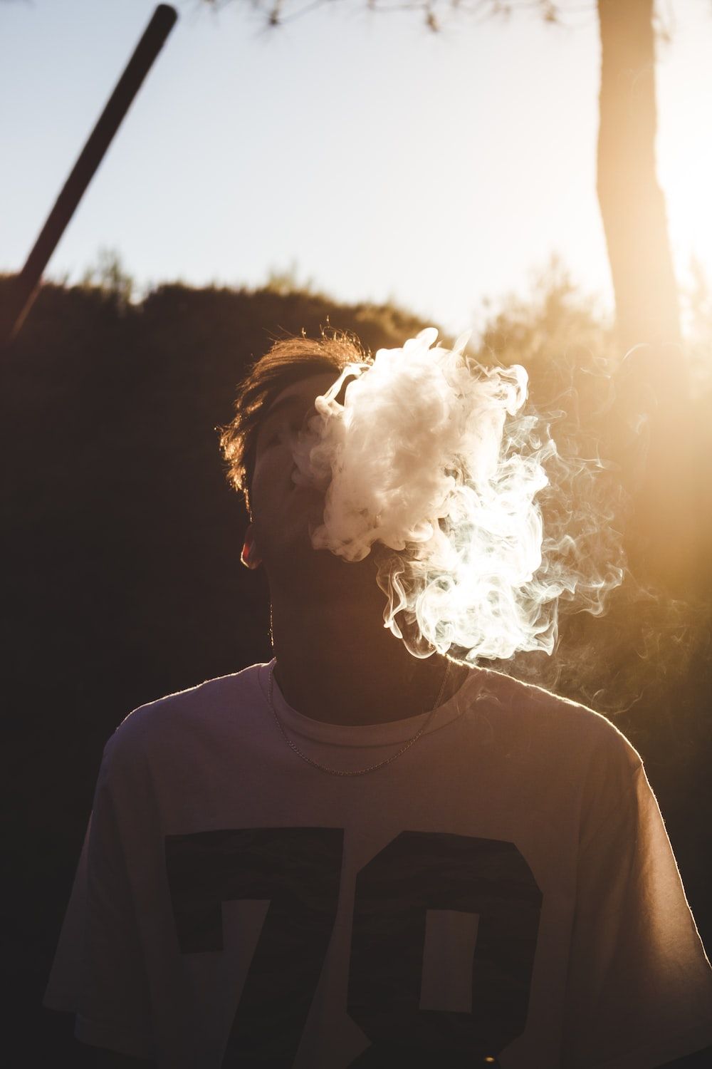 A man wearing a white shirt with black numbers on it exhales smoke. - Smoke
