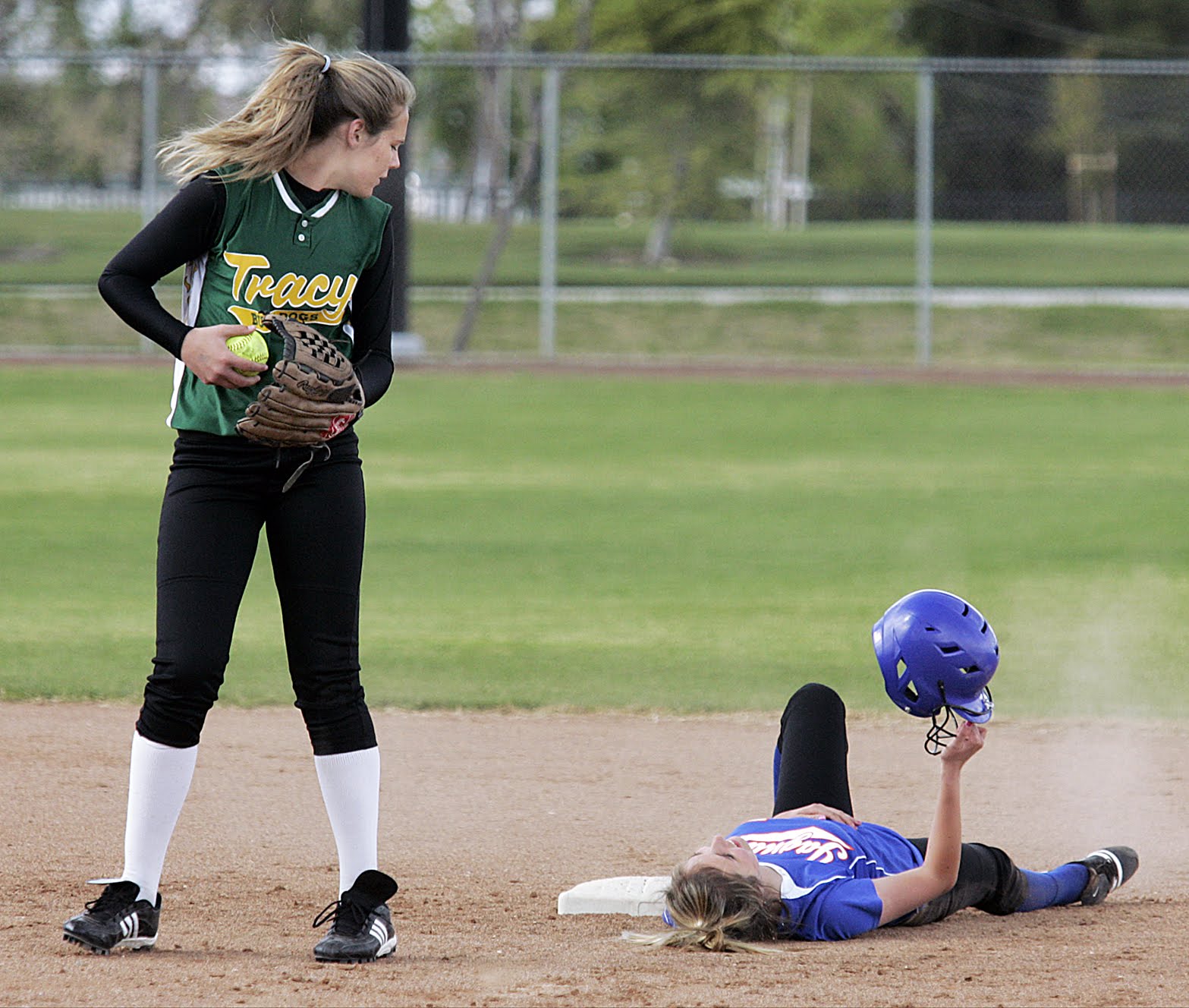 A woman is sliding into a base while another woman stands over her with a softball in her glove. - Softball