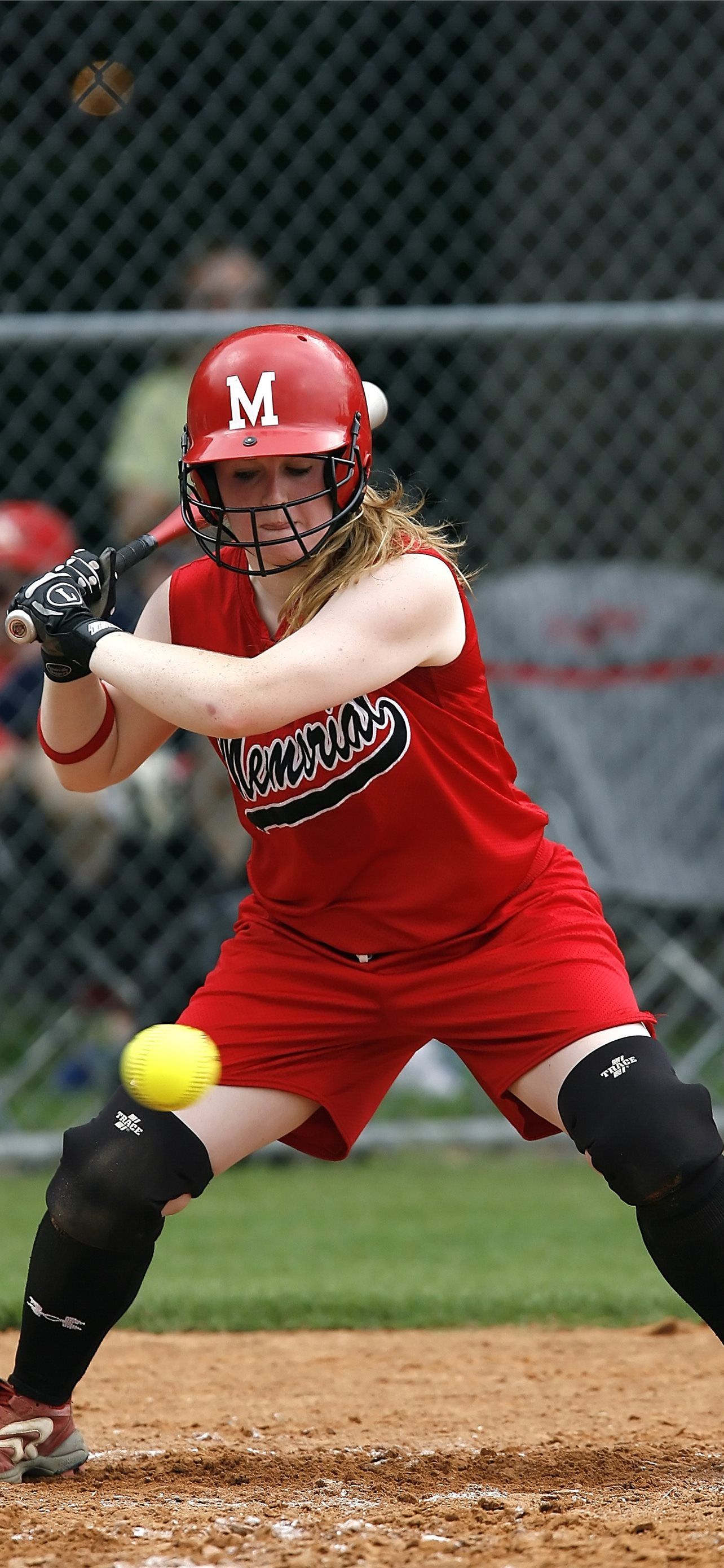A softball player in a red uniform swings at a ball. - Softball