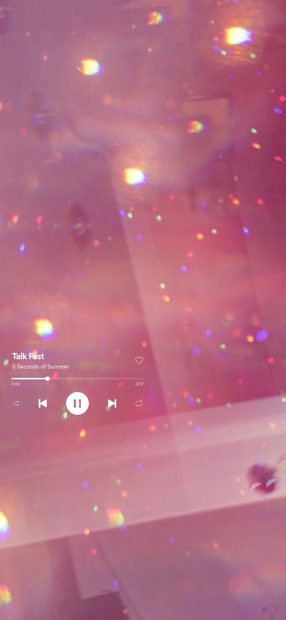 A screen shot of a pink background with rainbow light reflections and a music player in the bottom left corner. - Spotify