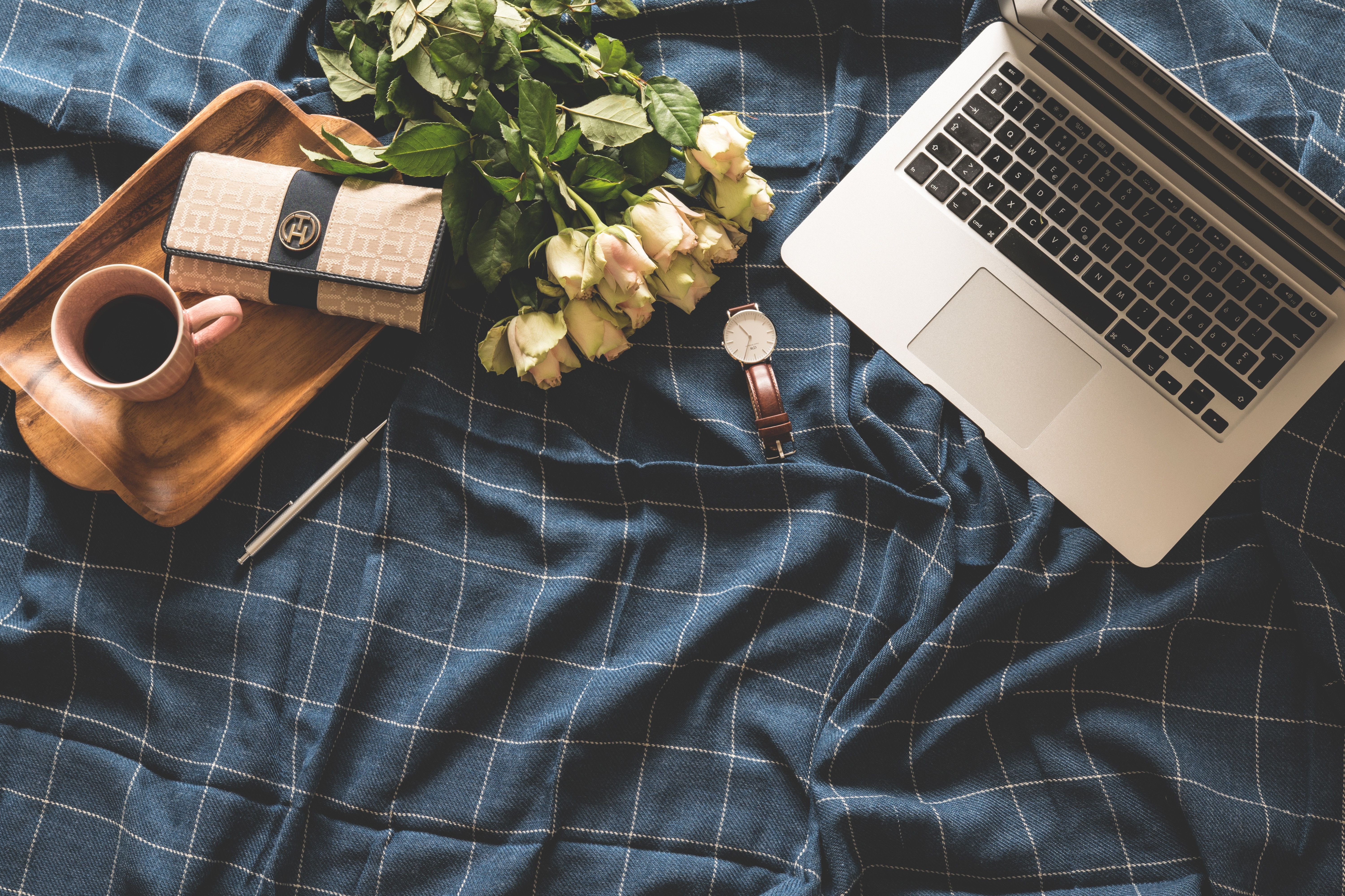 A laptop, a cup of coffee, a watch, a book, a pencil, and a bouquet of roses are placed on a bed. - Study