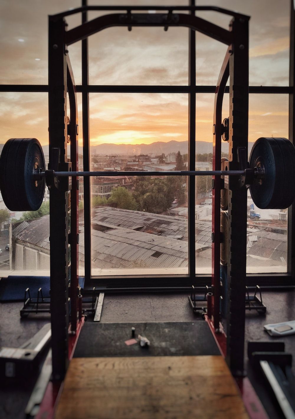 A sunrise through a window in a gym with a barbell in the foreground - Gym