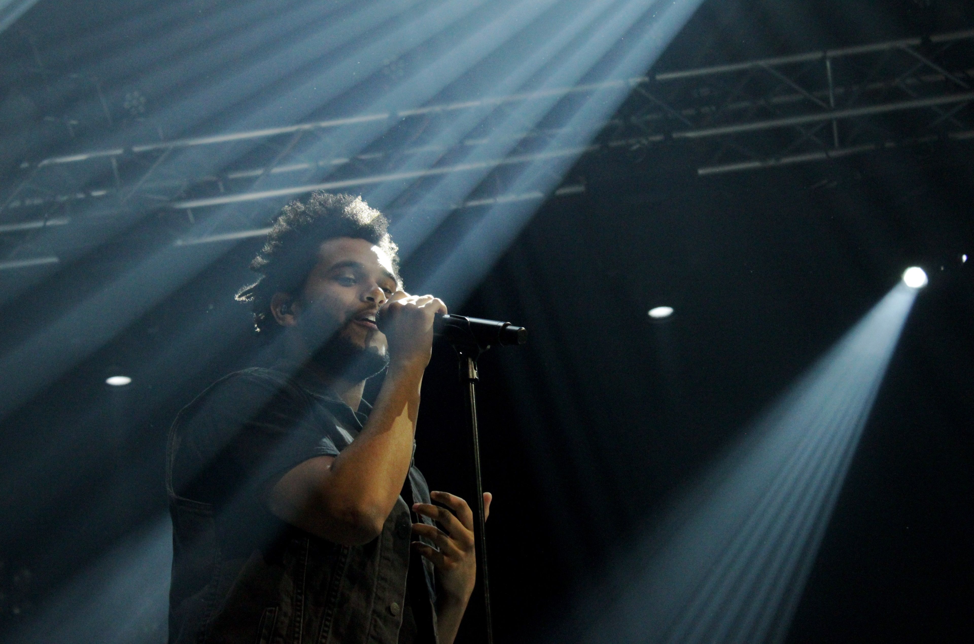 A man singing into microphone with lights shining on him - The Weeknd