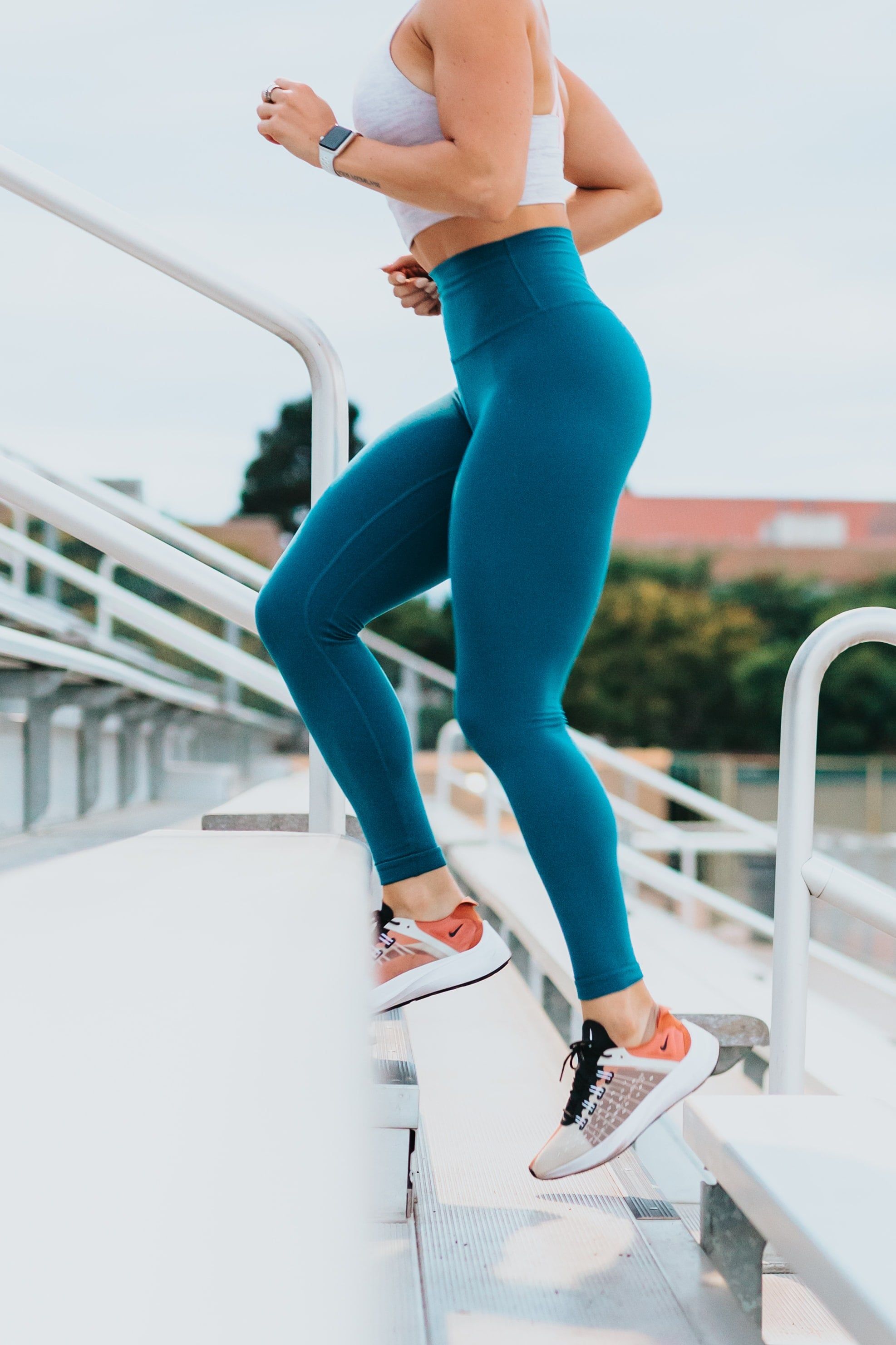 A woman in blue leggings and a white sports bra is running up the stairs. - Gym