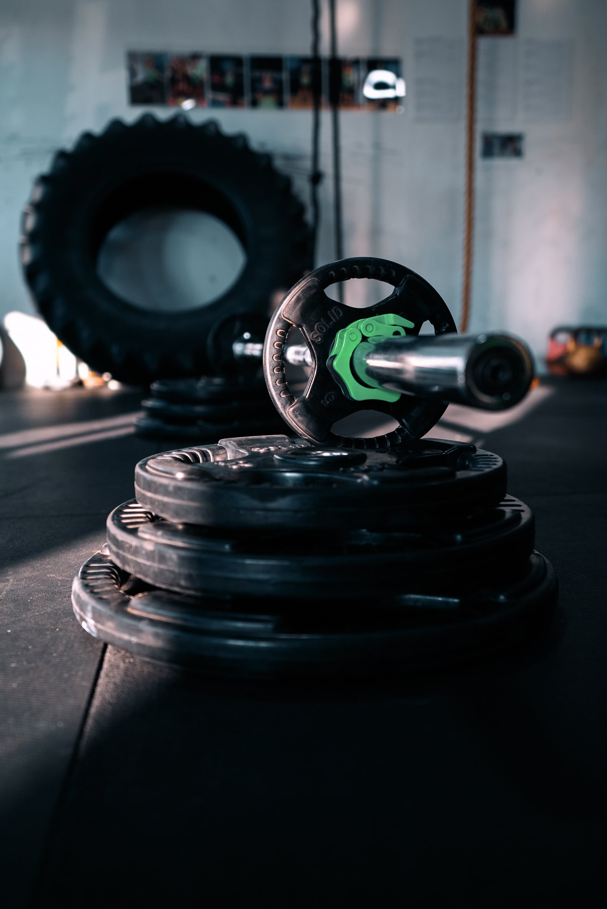 Barbell plates on a gym floor with a tire in the background. - Gym