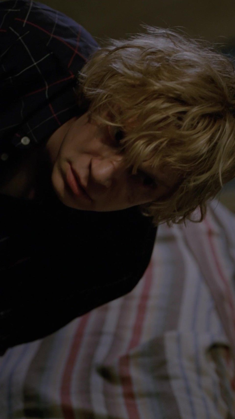 A blonde boy in a black shirt and red plaid jacket looks down at the camera. - Evan Peters