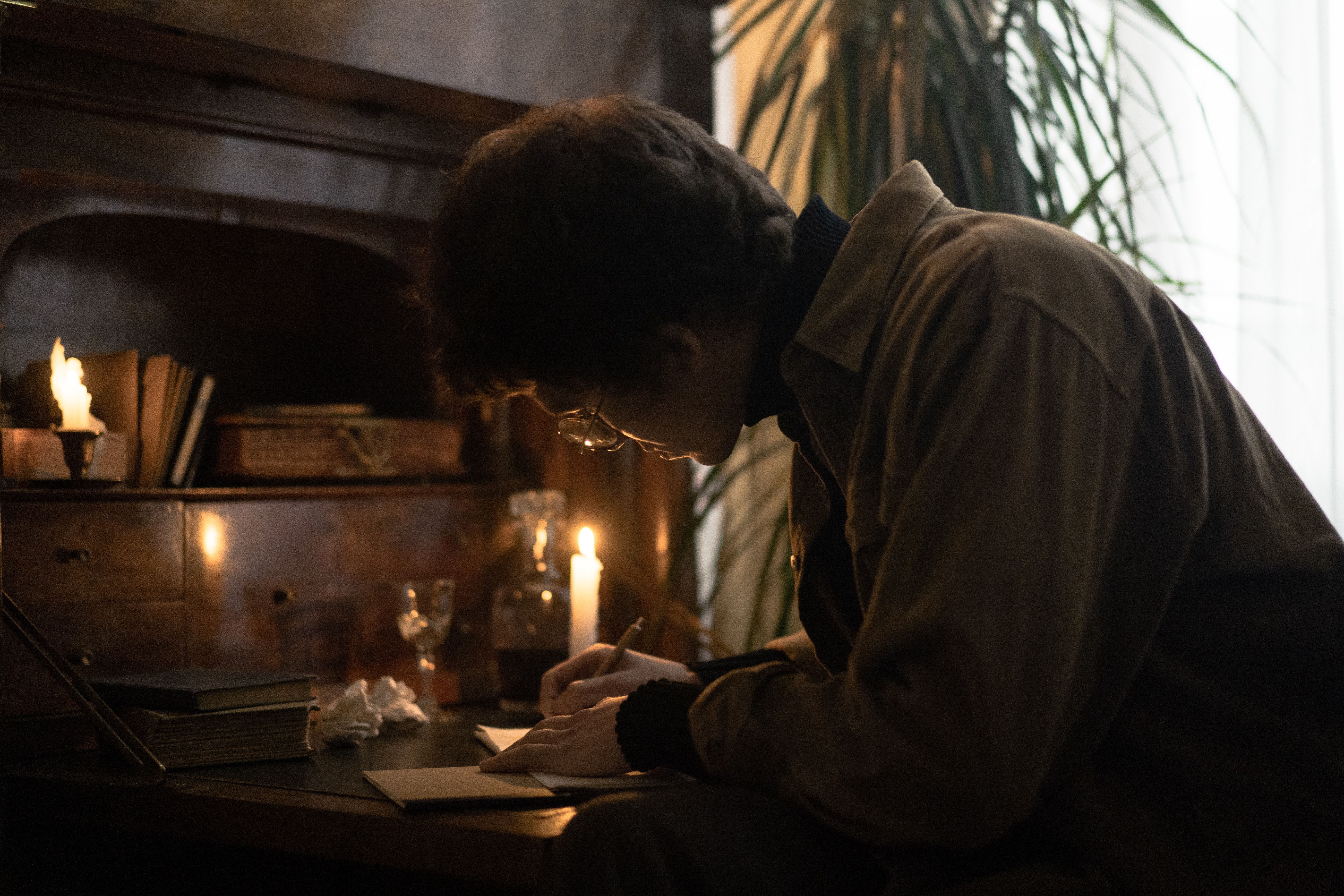 A man writing in a journal by candlelight. - Dark academia