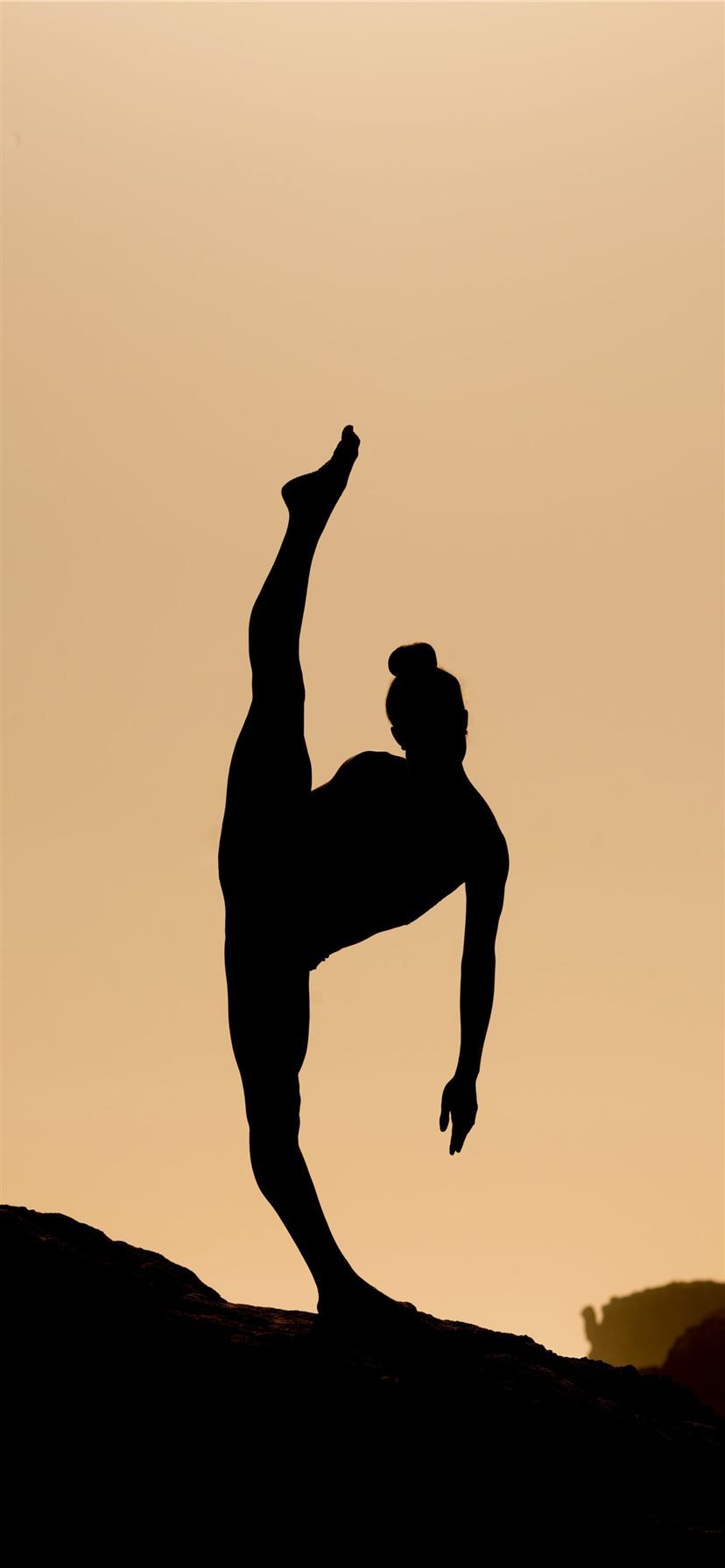 A silhouette of a man doing a one-handed handstand against a sunset sky - Dance