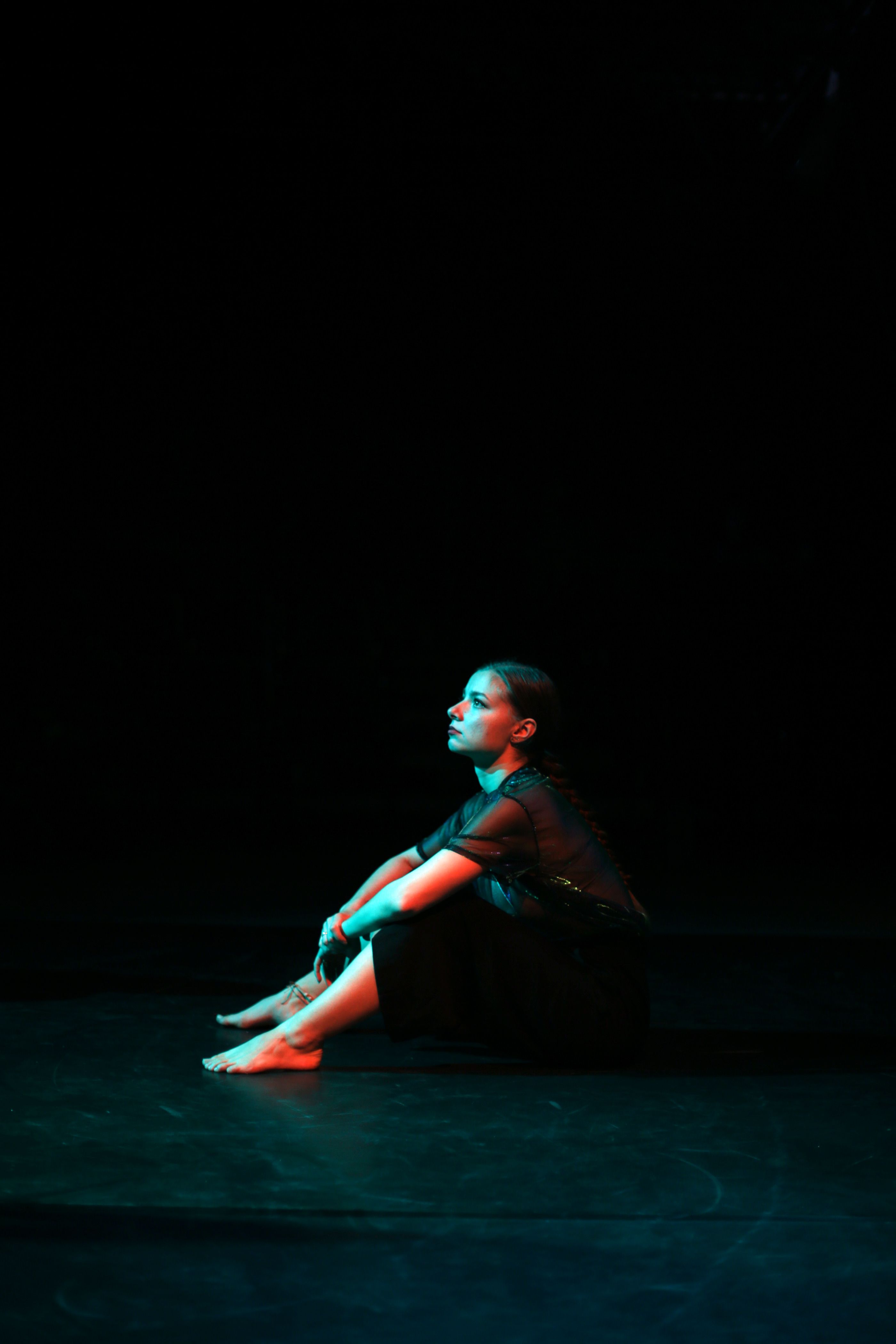 A woman sits on the floor in a dark room, bathed in red light. - Dance