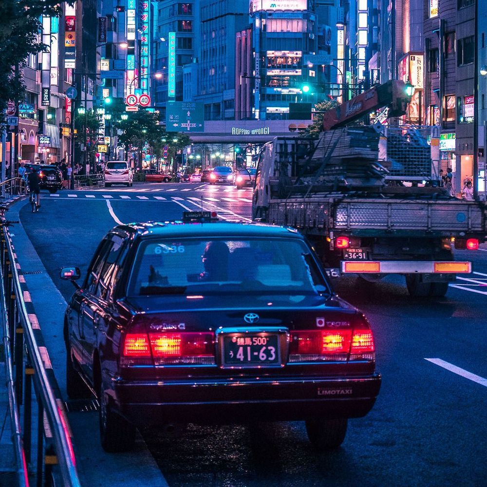 A taxi cab driving down a busy city street at night - JDM