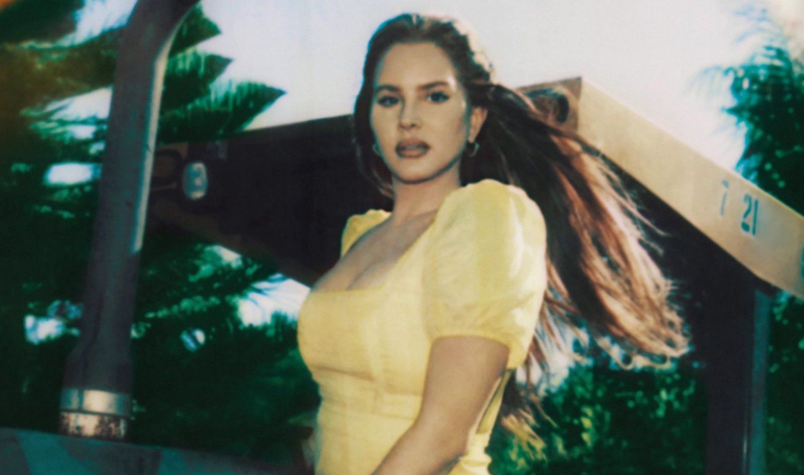 A woman in a yellow dress standing in front of a TV - Lana Del Rey