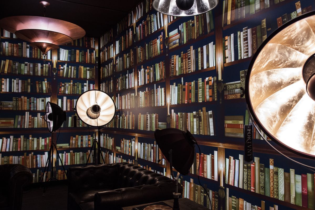 A room with a wall of bookshelves and three lamps. - Library