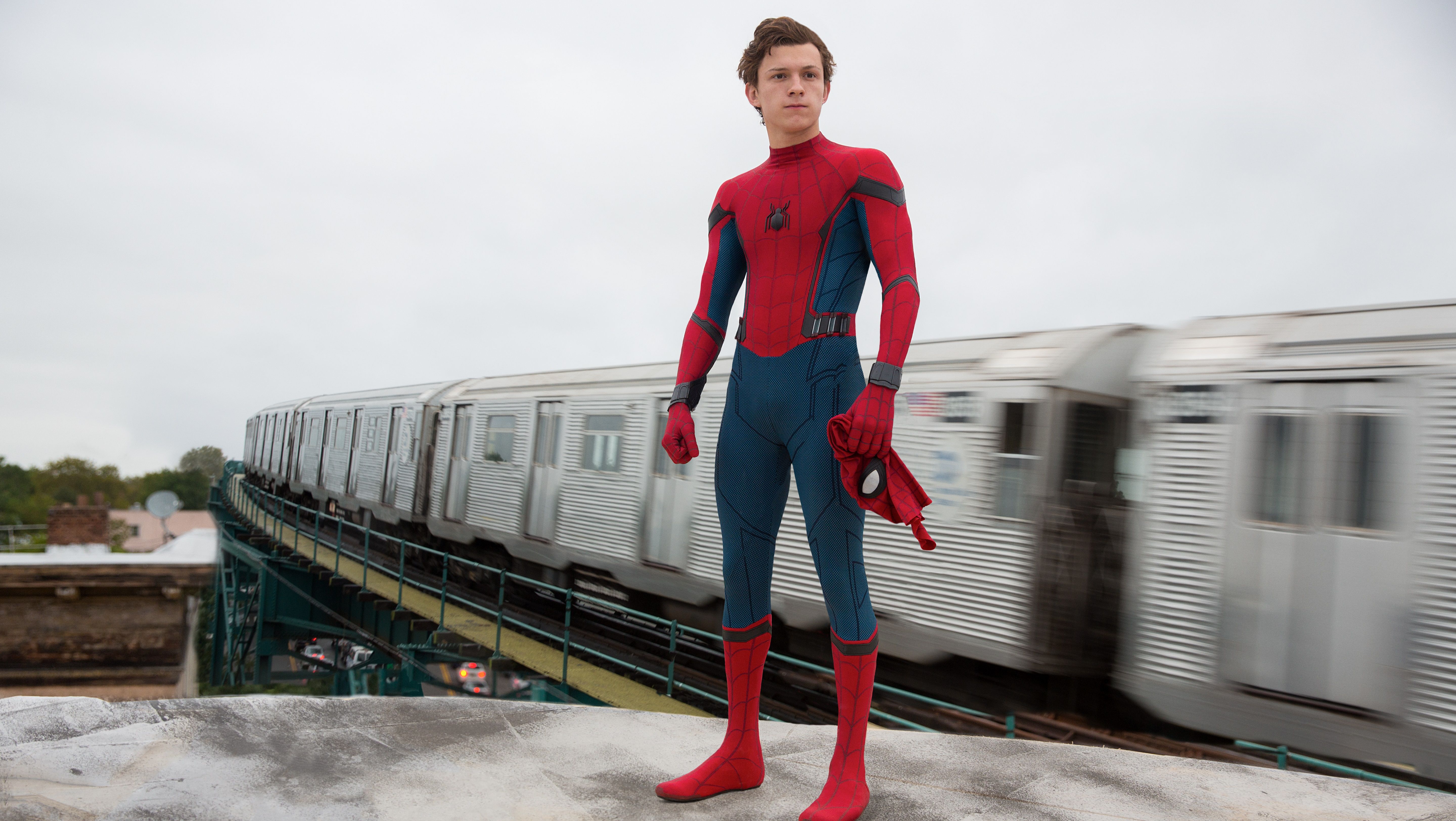 A young man in spiderman costume standing on the side of train tracks - Tom Holland