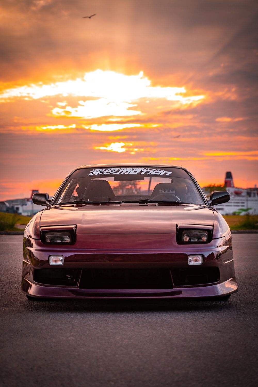 A maroon colored car parked on the road with a sunset in the background - JDM