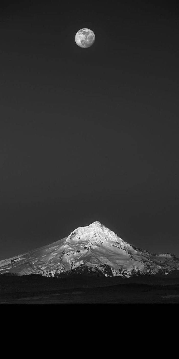 A black and white photo of the moon over snow covered mountains - Black