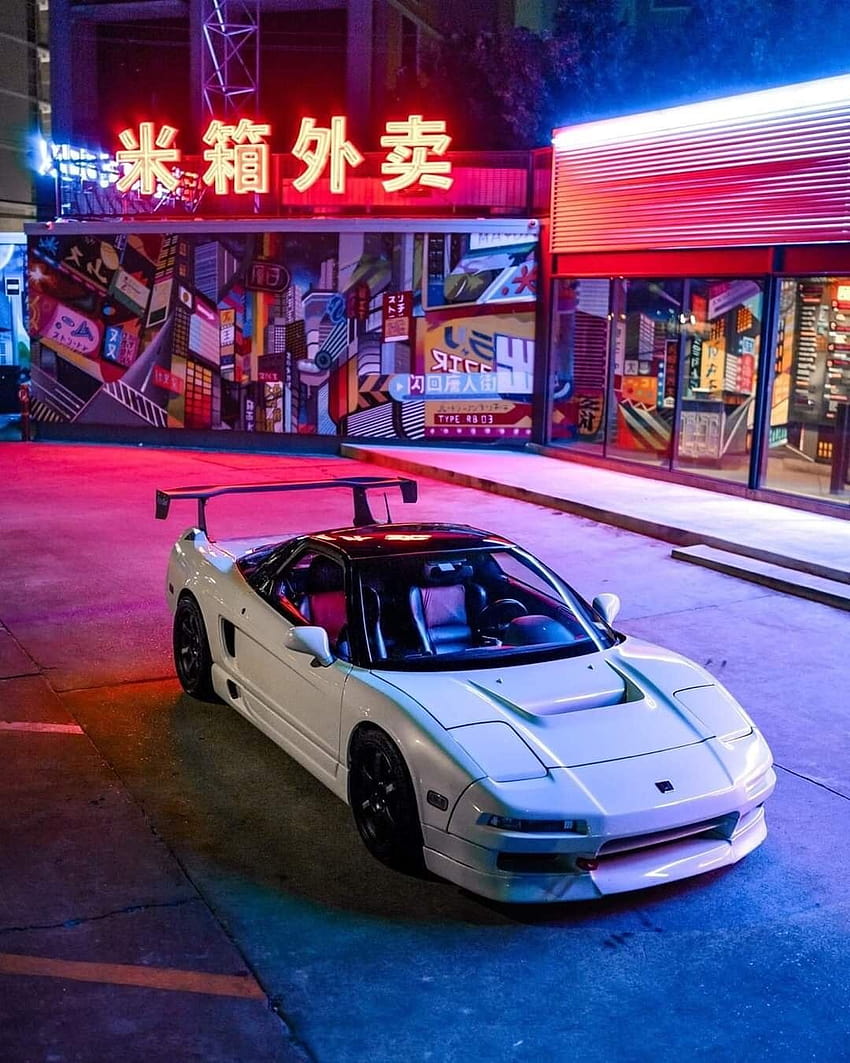 A white NSX with aero parts, parked on the roadside in front of a shop with a neon sign that reads 