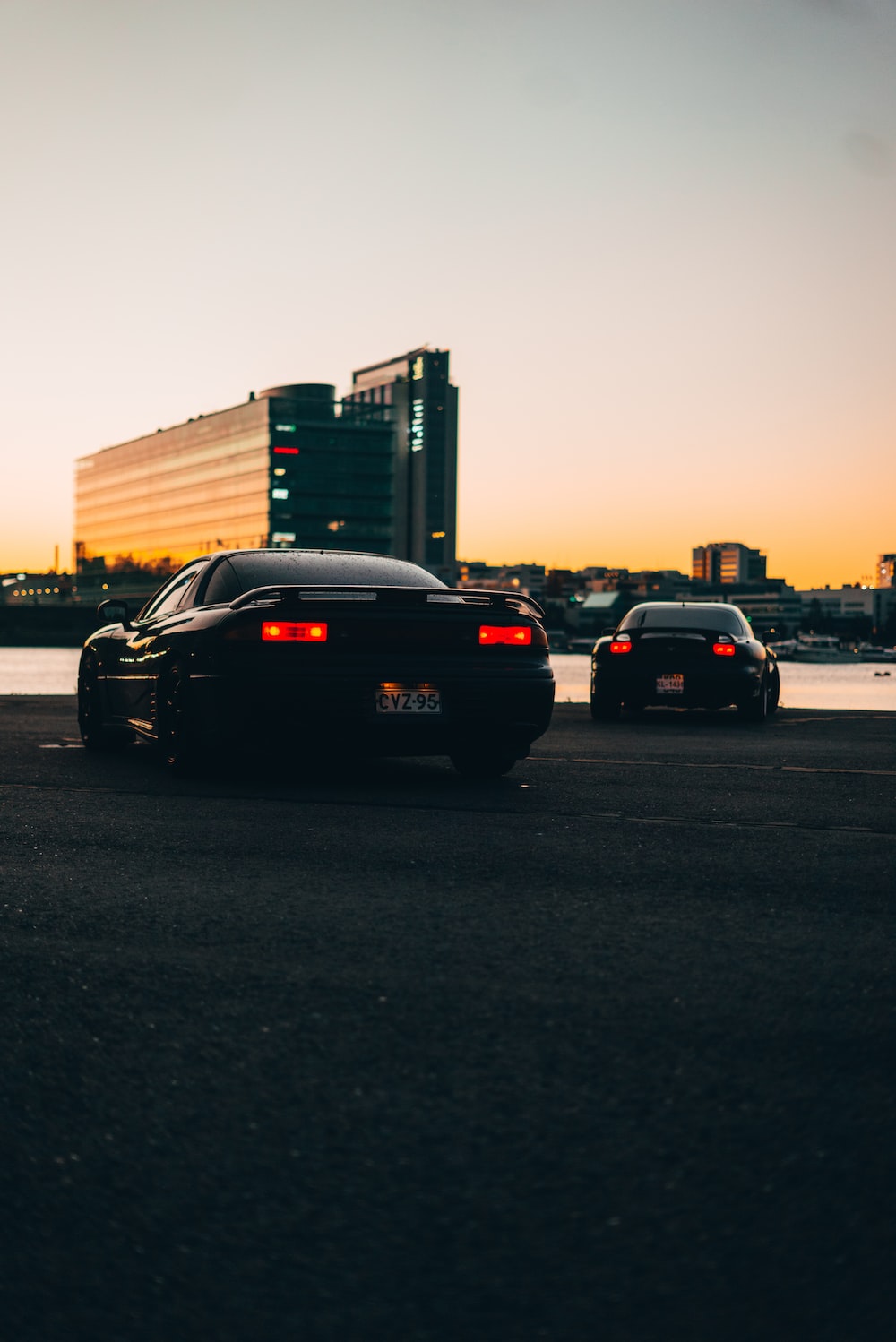 Two cars parked in a parking lot with a city skyline in the background - JDM