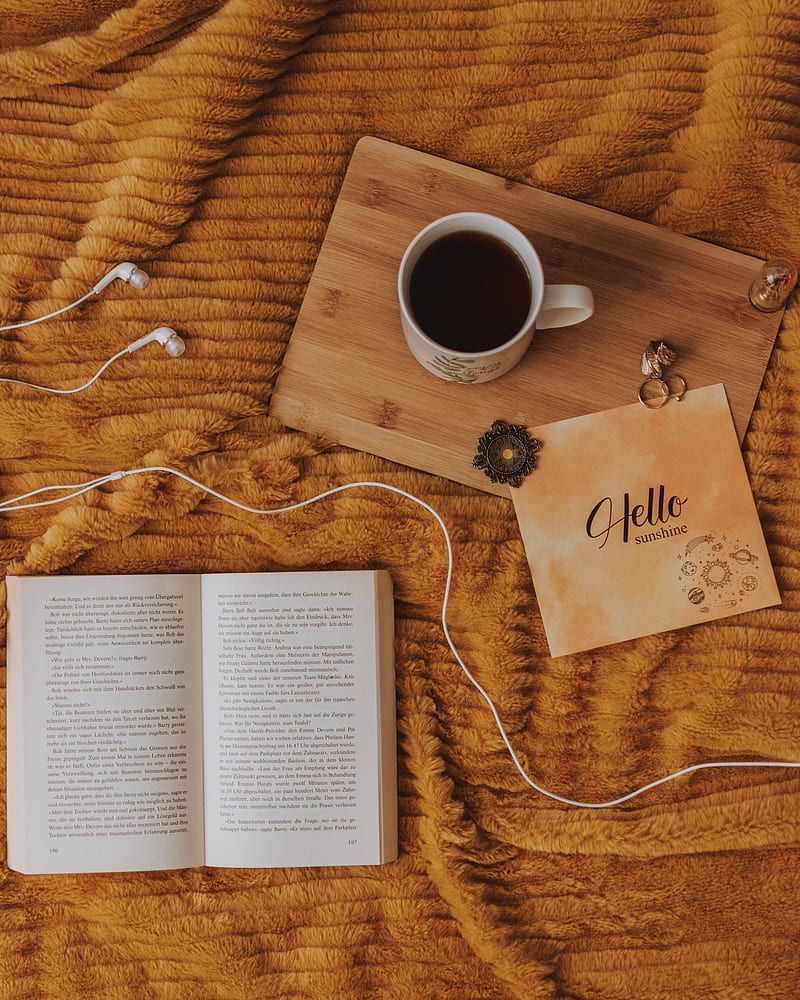 A book, a cup of coffee, and some earphones on a bed. - Coffee