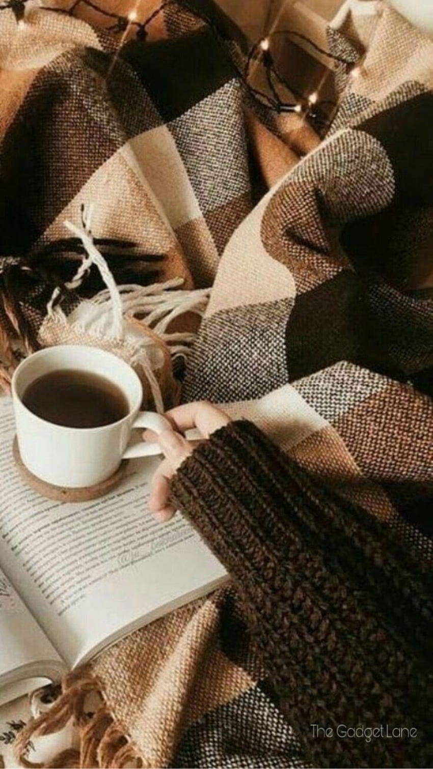 A person sitting on the bed with their hands holding onto an open book and coffee - Coffee